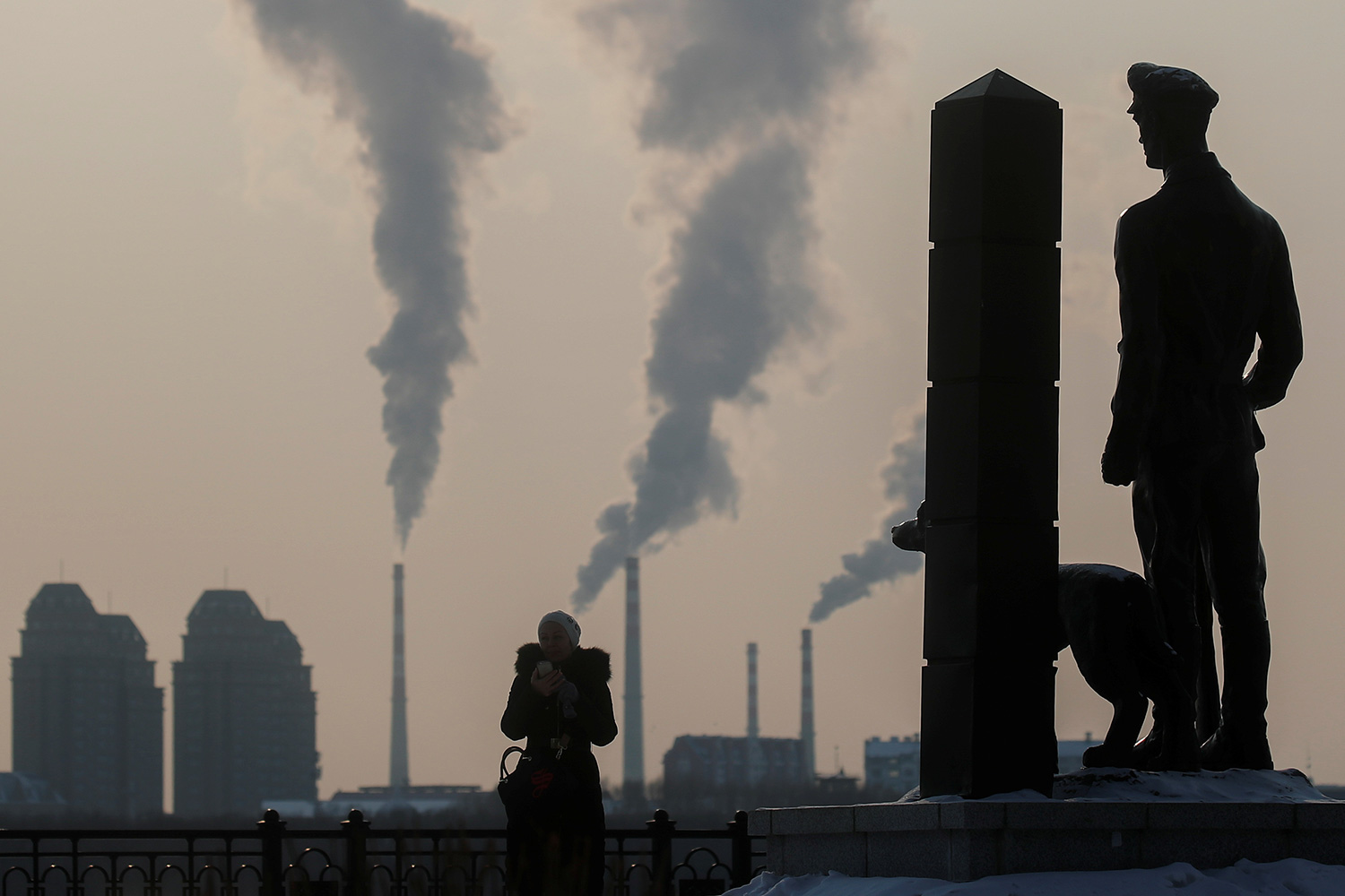This is a striking photo with the woman, her dog, and the statue all silhouetted against factories belching out smoke across the border.