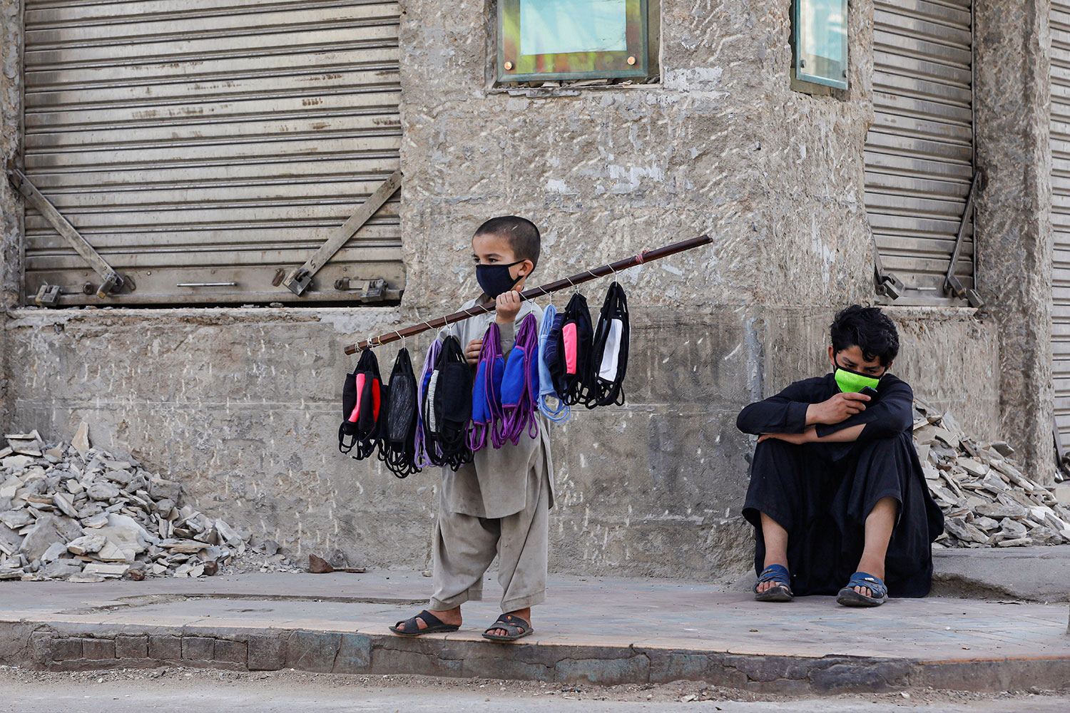 Photo shows the boy wearing a mask with several more tied around a stick as he advertises his wares.