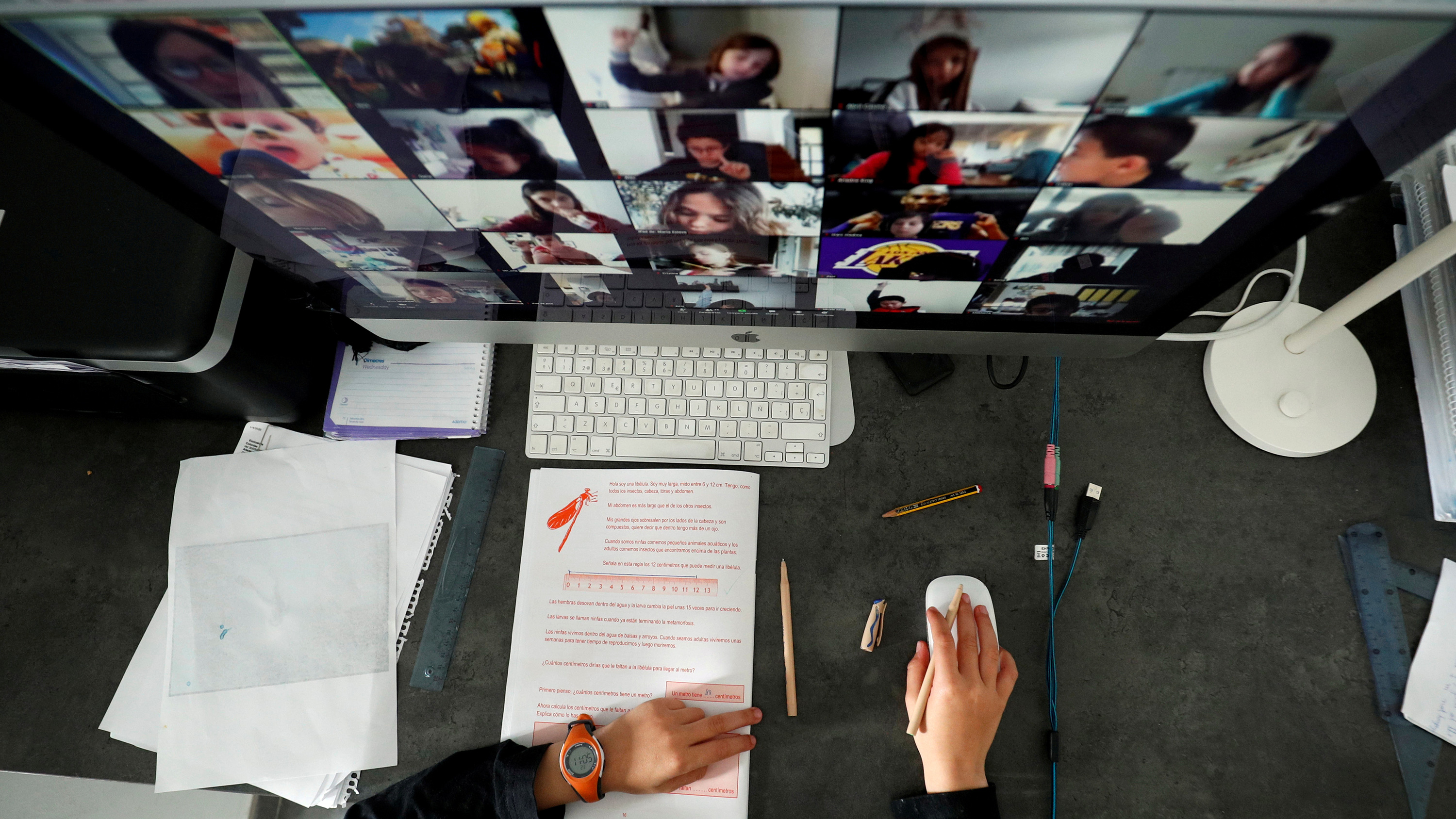 The photo shows a large screen seen from above with the faces of lots of students at remote locations.