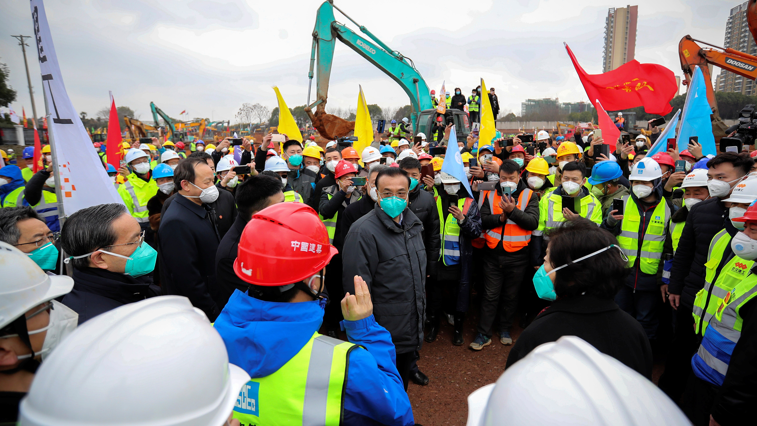 Photo shows the leader surrounded by construction workers and other people at the construction site with huge cranes looming in the background.