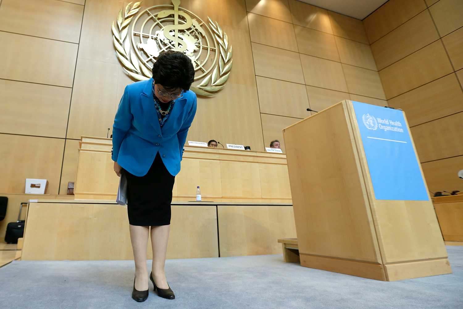 The photo shows Chan at the front of the auditorium bowing to the assembly.