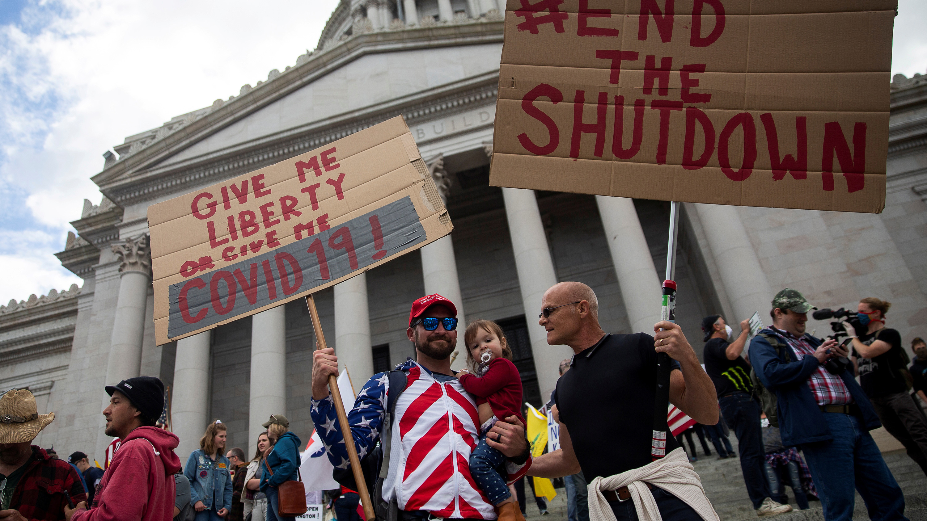 The protestors hold signs calling for the end of the shutdown. One of them wears an American flag jacket.