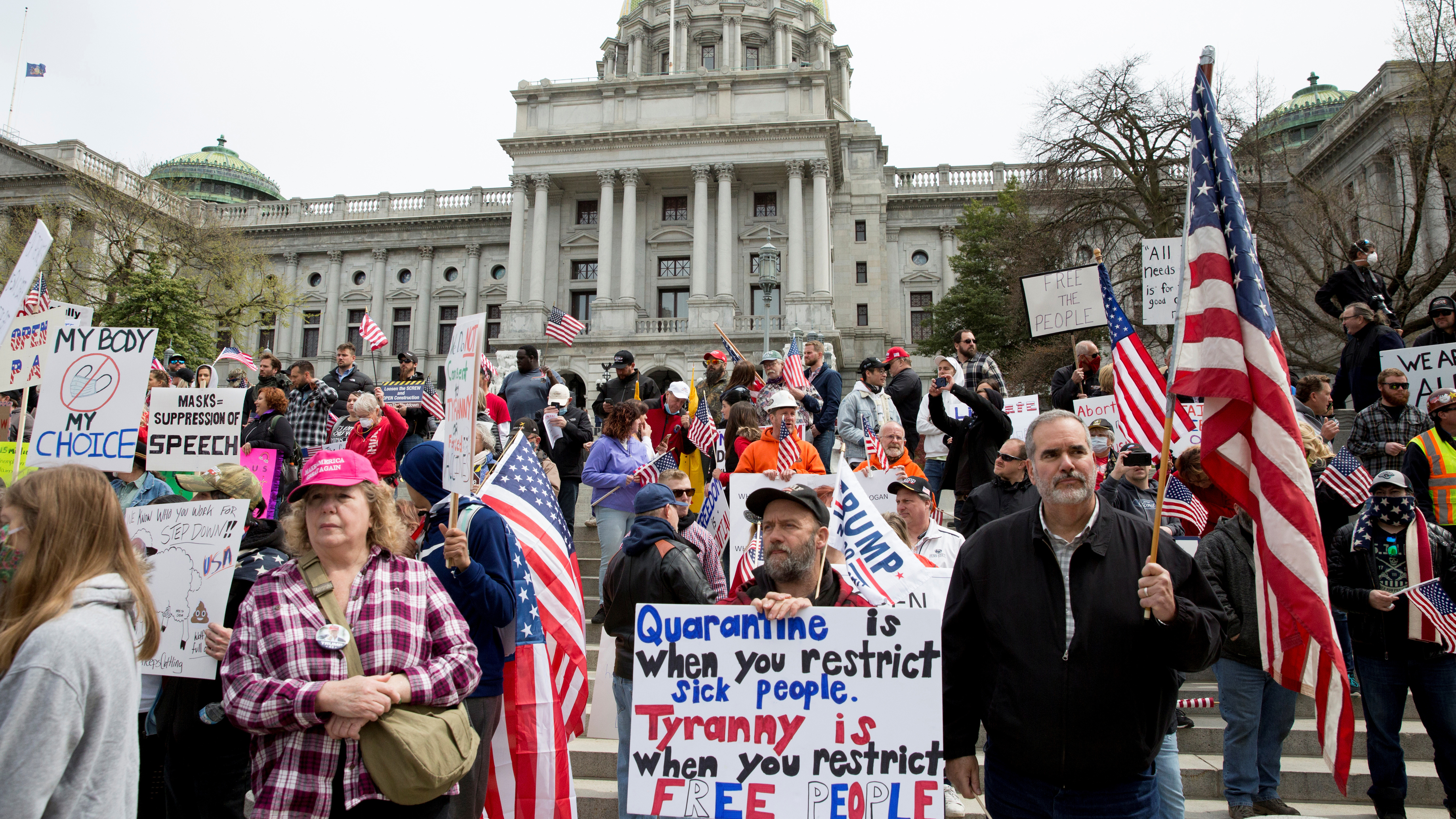 The photo shows a large number of protestors holding signs and waving the American flag on the steps of what appears to be the PA state house. Very few of them are wearing masks, and many of them are not practicing physical distancing.