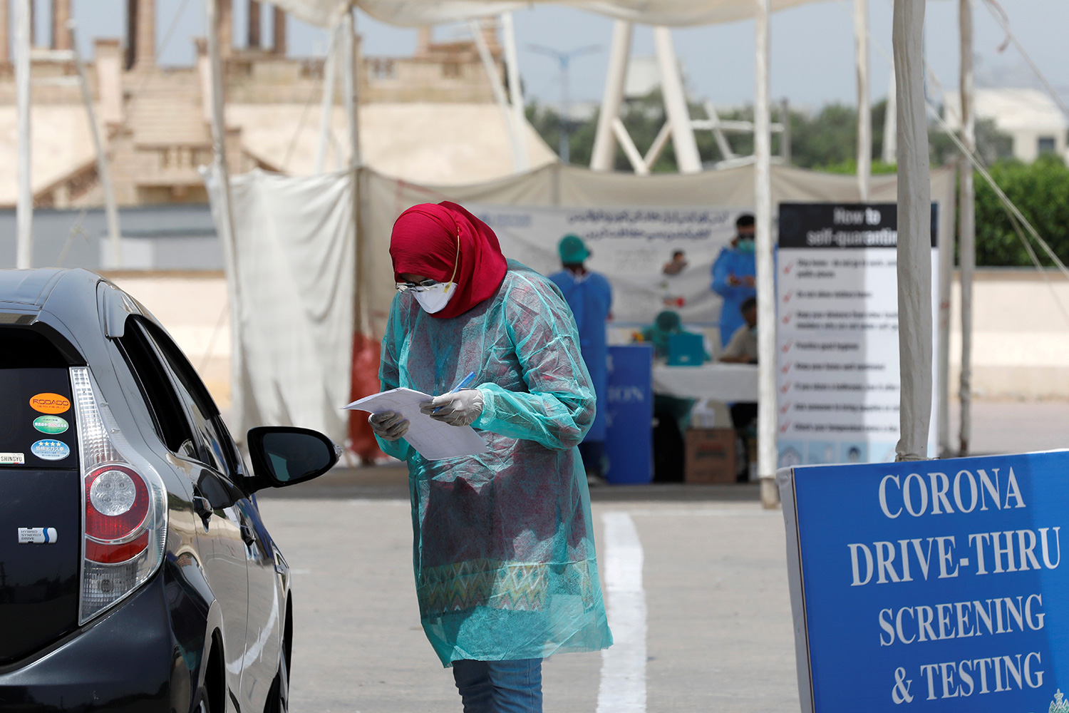 The photo shows a woman wearing protective gear attending to a driver of a vehicle.