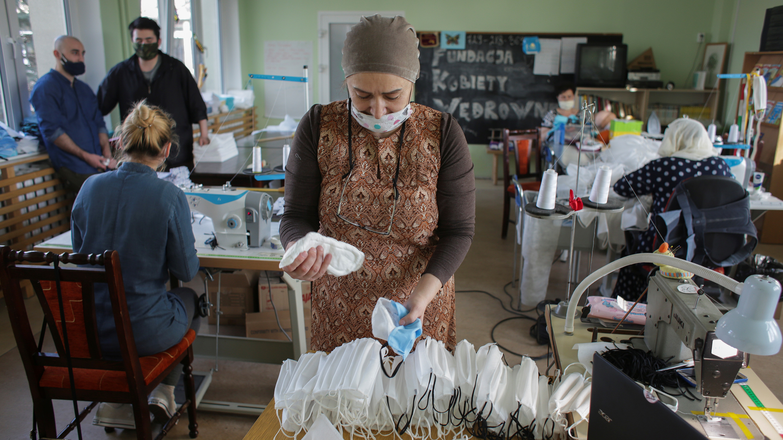 The picture shows a crowded workspace with several stations with sewing machines and a number of people assembling facemasks. Khedi Alieva and volunteers of the Nomadic Women Foundation have been sewing masks every day for twelve hours since March 17, 2020.
