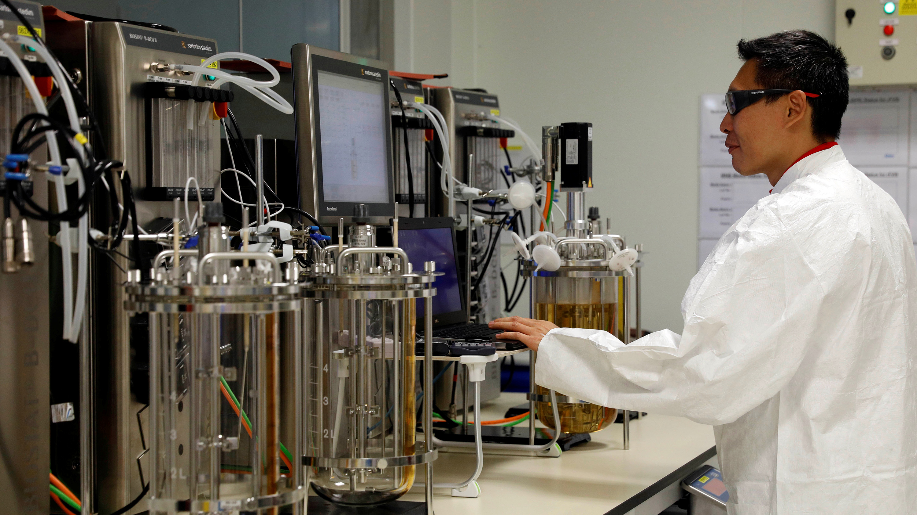 The photo shows a worker at a lab bench.