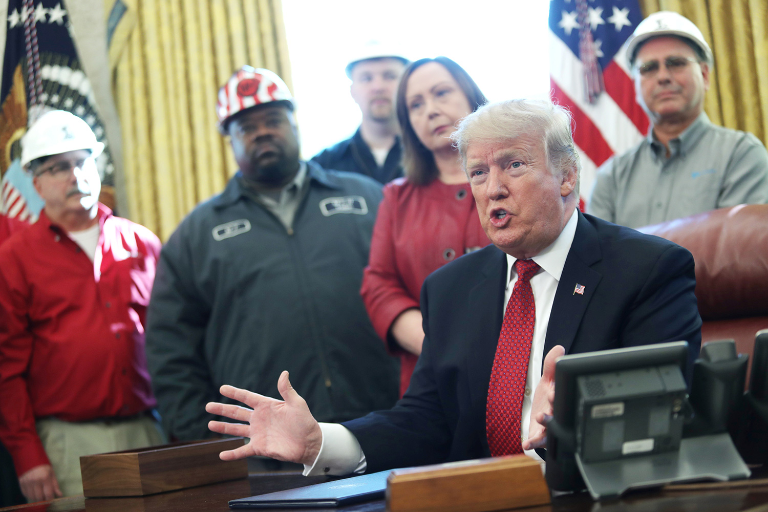 The photo shows President Trump speaking with several people wearing hard hats standing behind him.