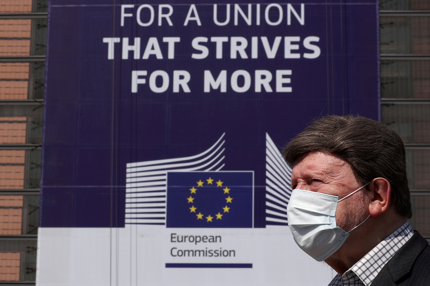 The man is wearing a face mask and passing a sign that reads, "FOR A UNION THAT STRIVES FOR MORE."