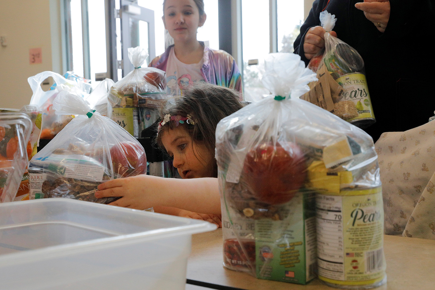 The photo shows a cute little girl examining bags filled with various foodstuffs.