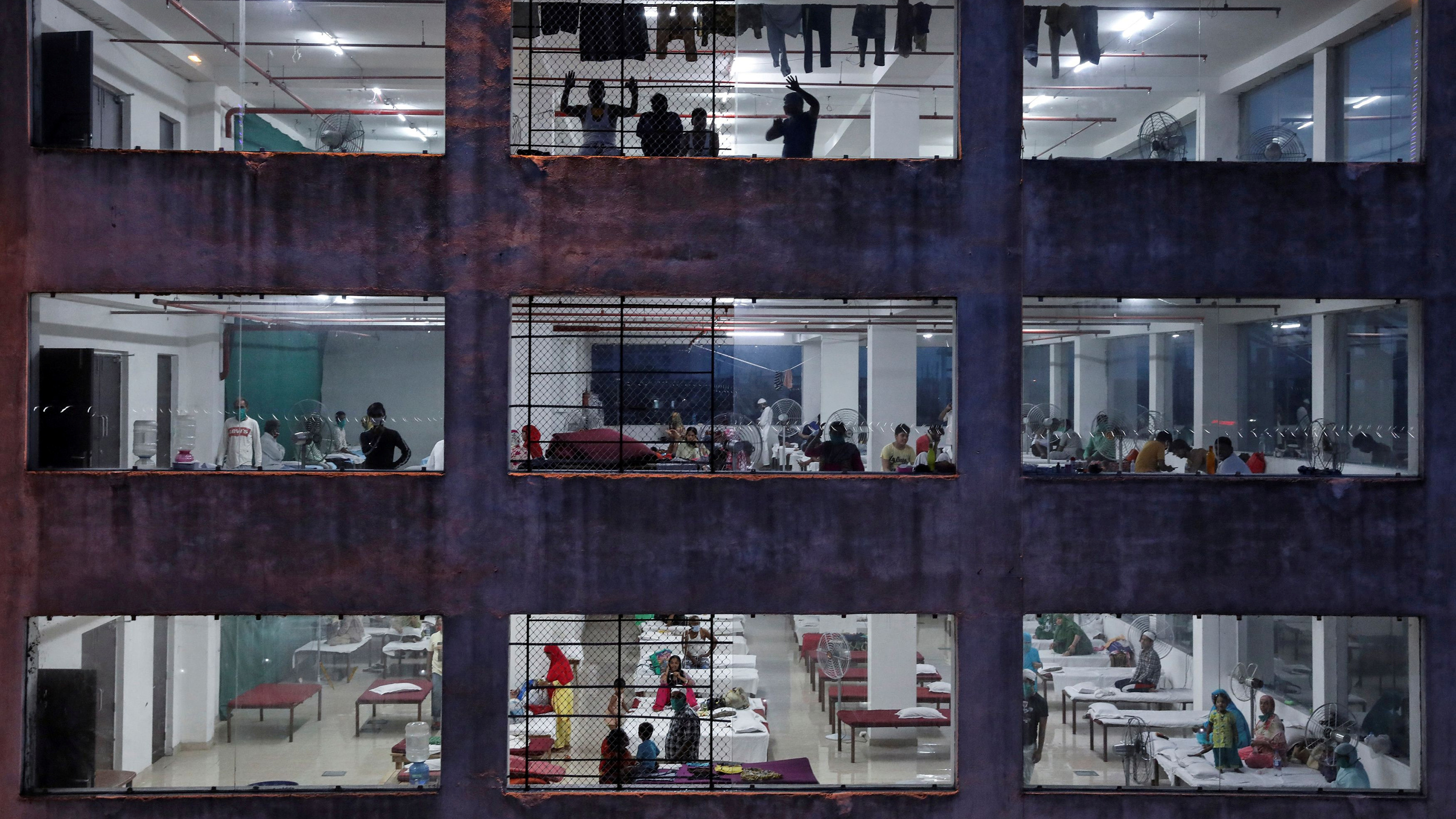 The photo shows the façade of a modern building with several large rectangular windows looking in on people on beds.
