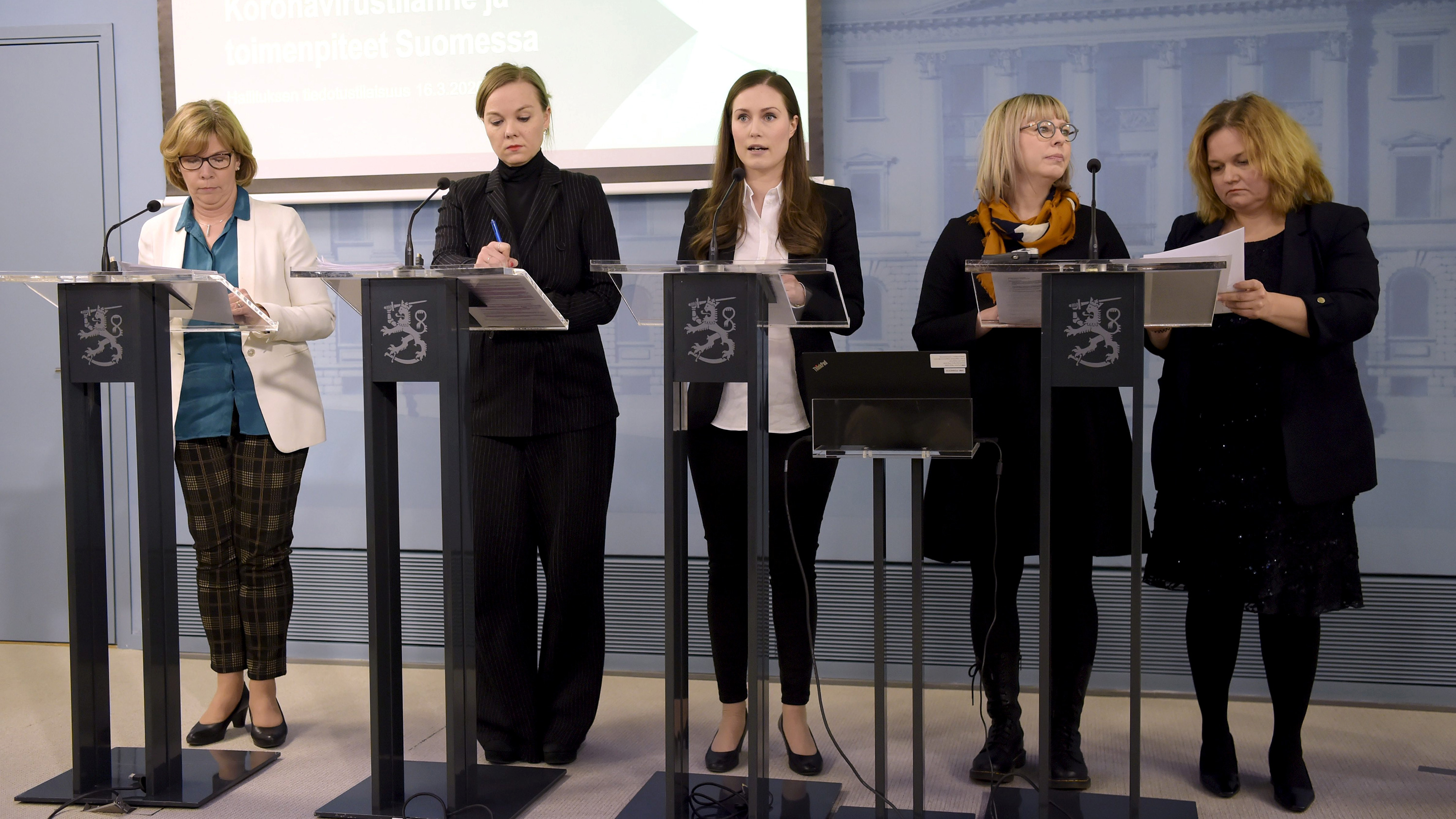 The photo shows the prime minister speaking into a microphone at a podium flanked by government ministers.
