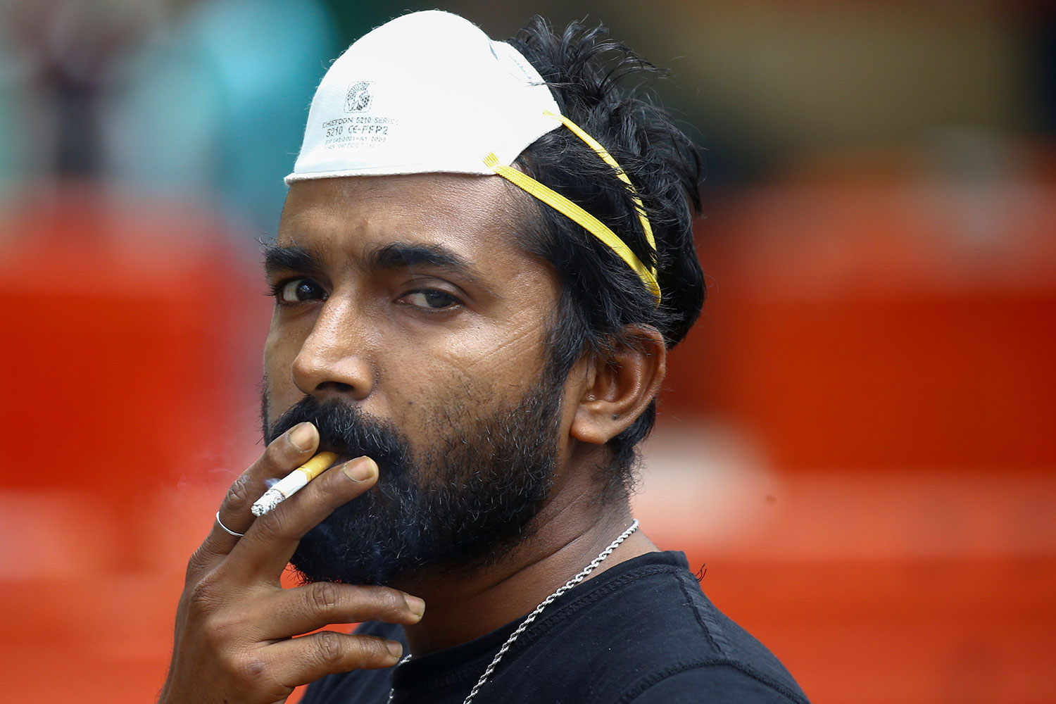 Image shows a man with a mask pushed up onto his forehead while he holds a cigarette to his lips.