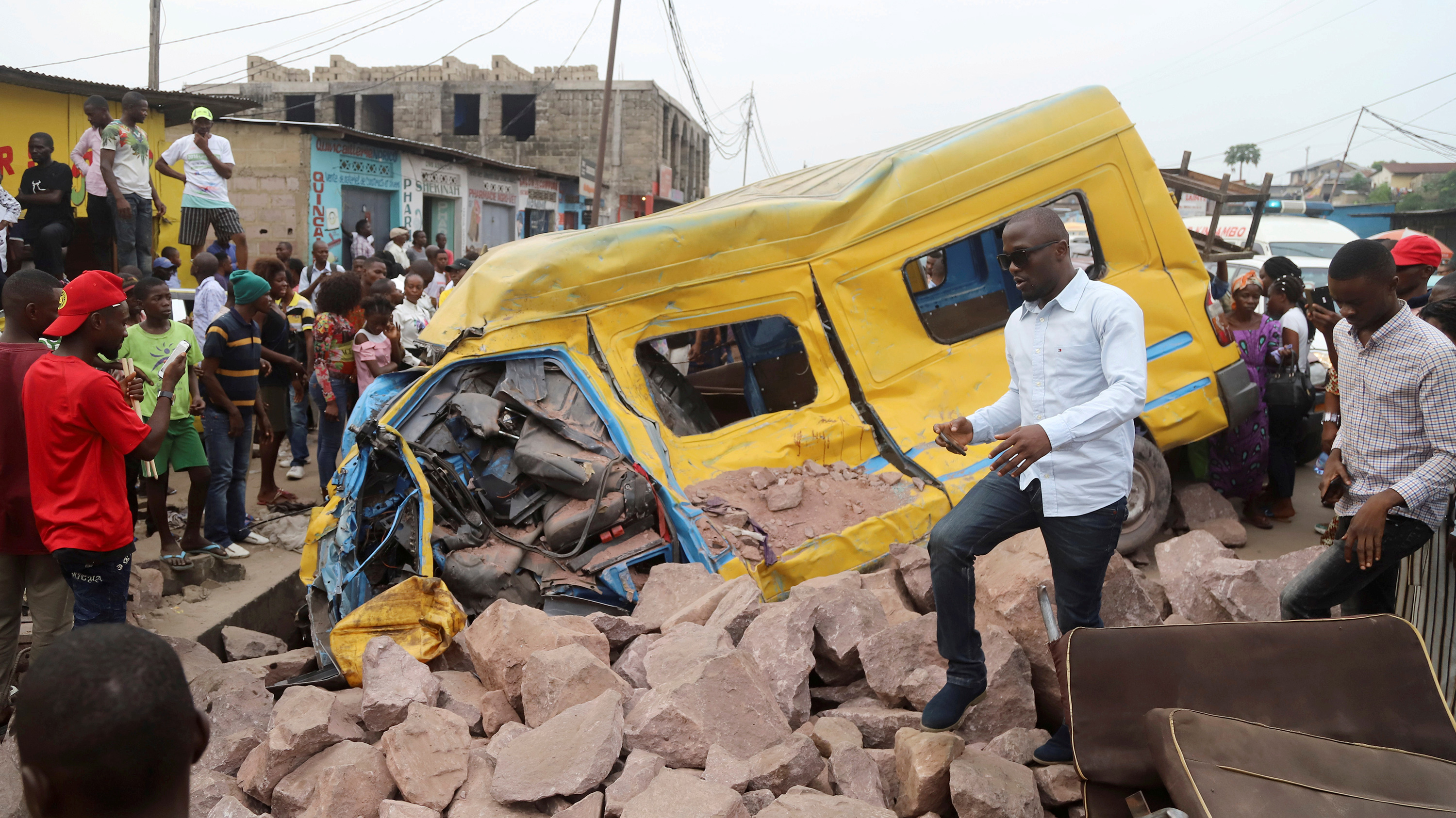 The image shows a yellow passenger bus wrecked in a pile of rubble.