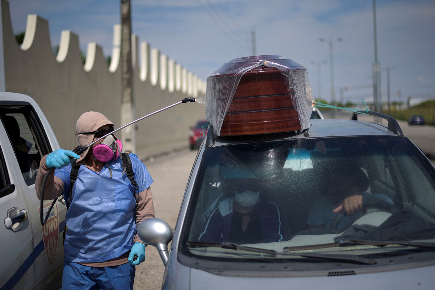 The photo shows a health worker in protective gear spraying a vehicle.
