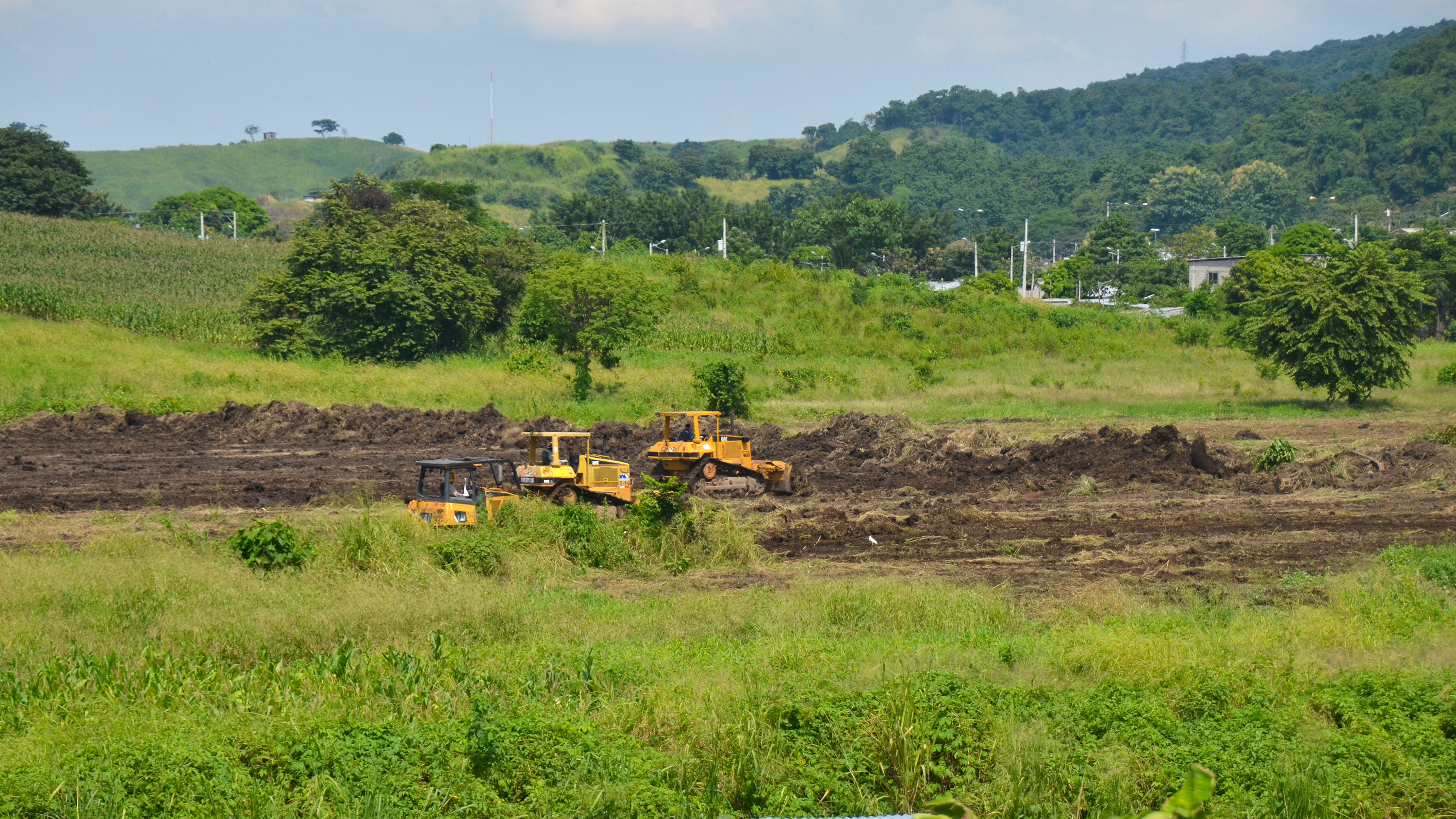 Picture shows a lush green landscape with some heavy machines clearing the ground.