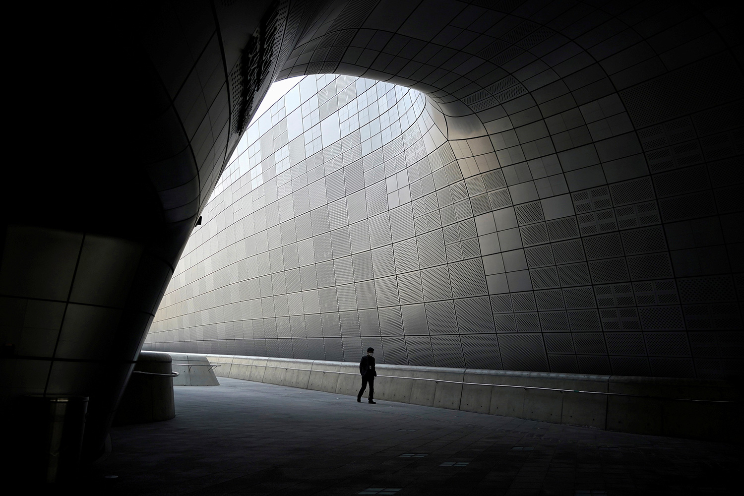 The image shows the tiny figure of a person walking along a huge corridor all by himself.