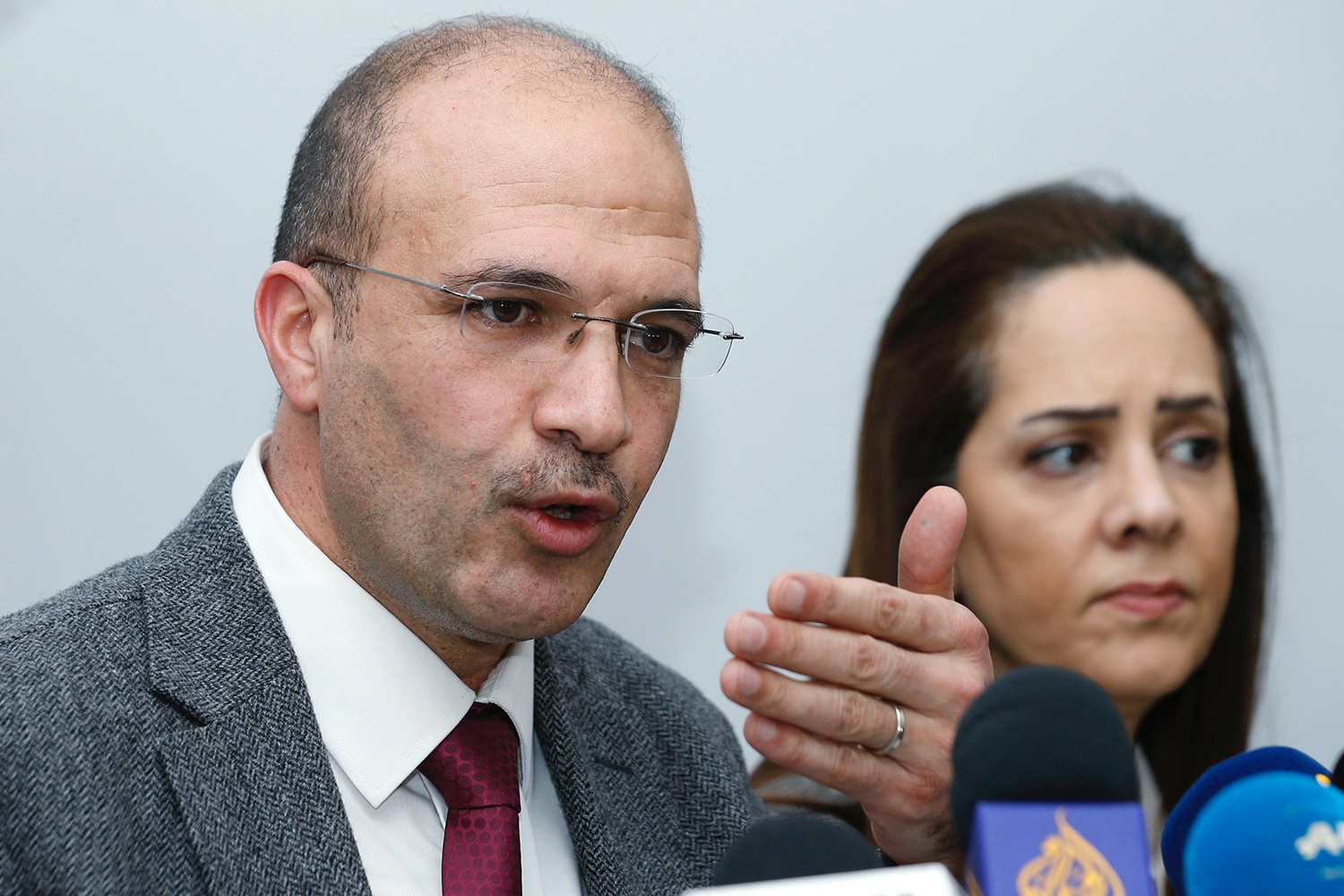 The photo shows the minister standing at a podium speaking into a microphone and gesturing with his hand while the WHO representative stands behind him with a concerned look on her face.