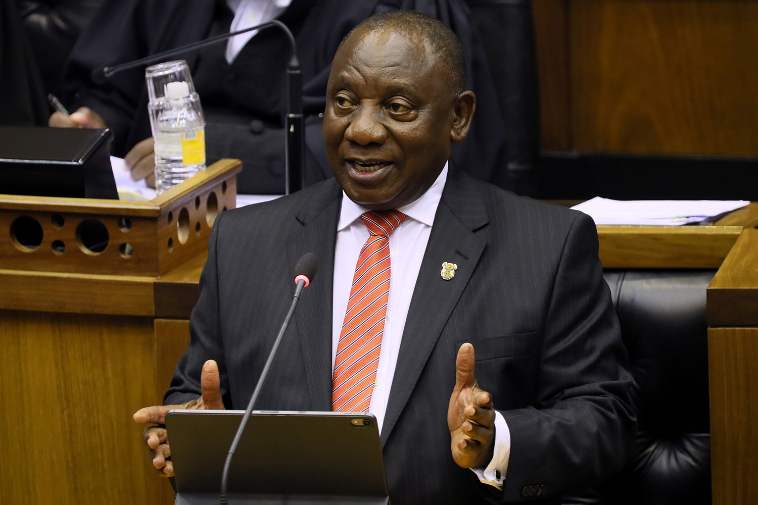 The photo shows the South African leader at a podium in a legislative house speaking and gesturing with his hands.