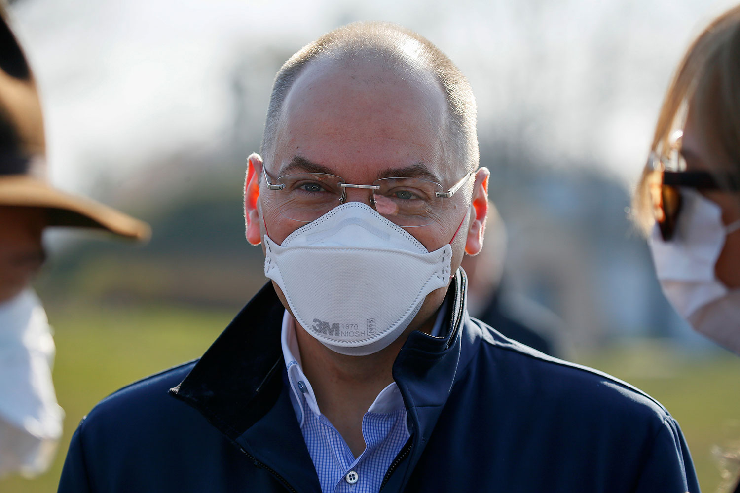 The photo shows the health minister on what appears to be a spring morning standing in the sun with two other people and wearing a mask.