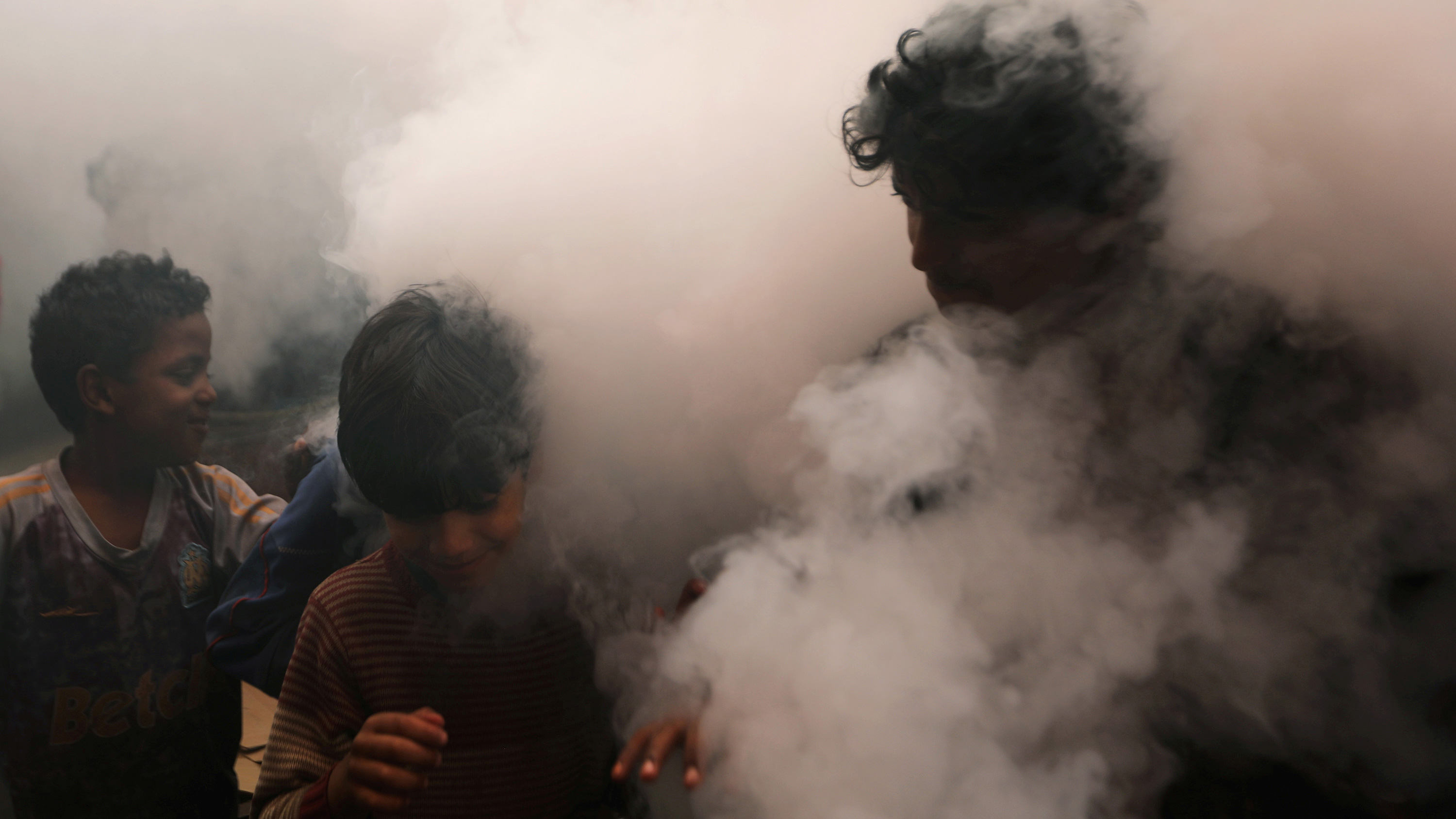 This is a powerful photo showing one man and two boys walking through a thick cloud of disinfectant mist.