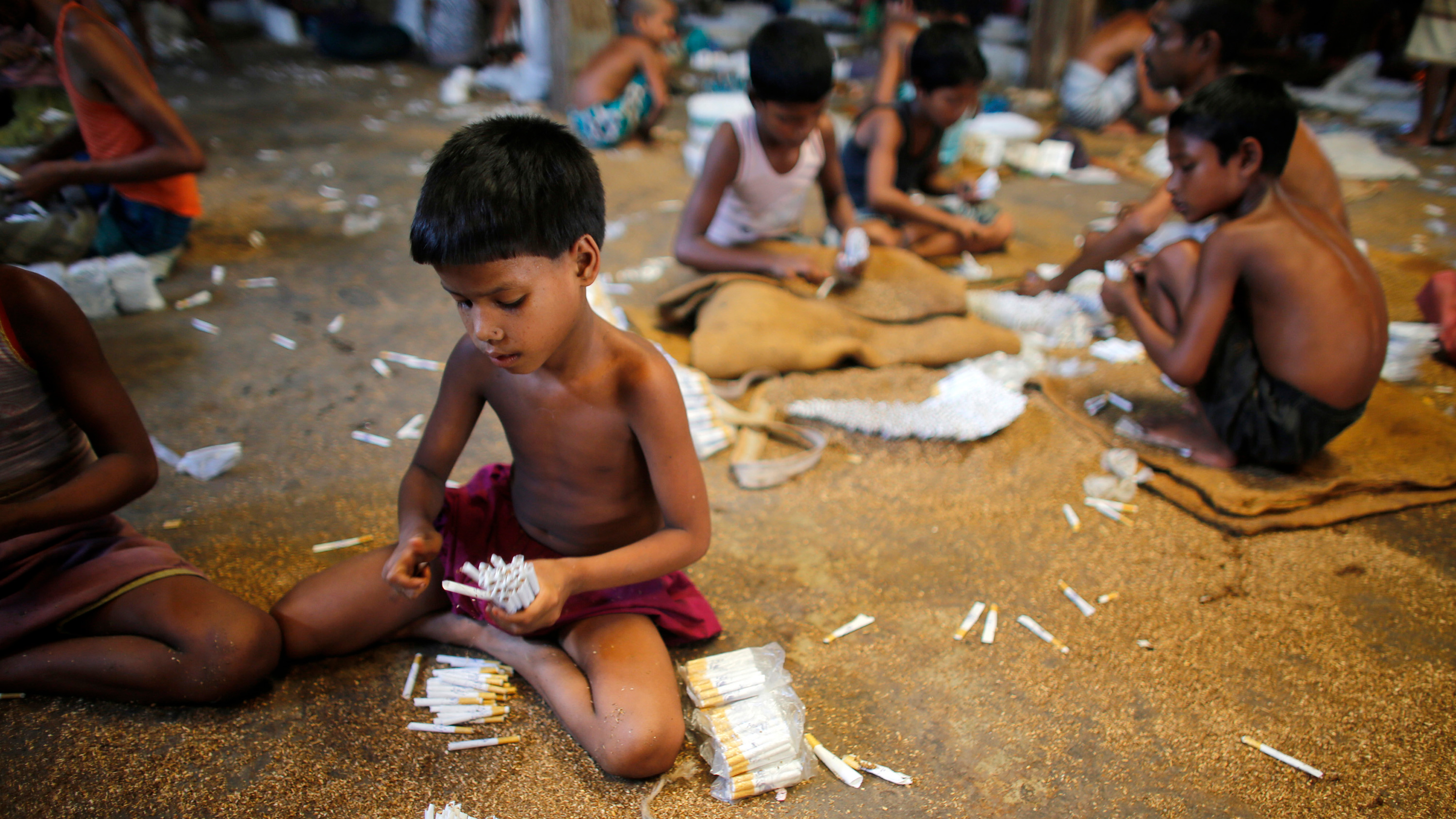 Picture shows several small children sitting around sorting piles of cigarettes.