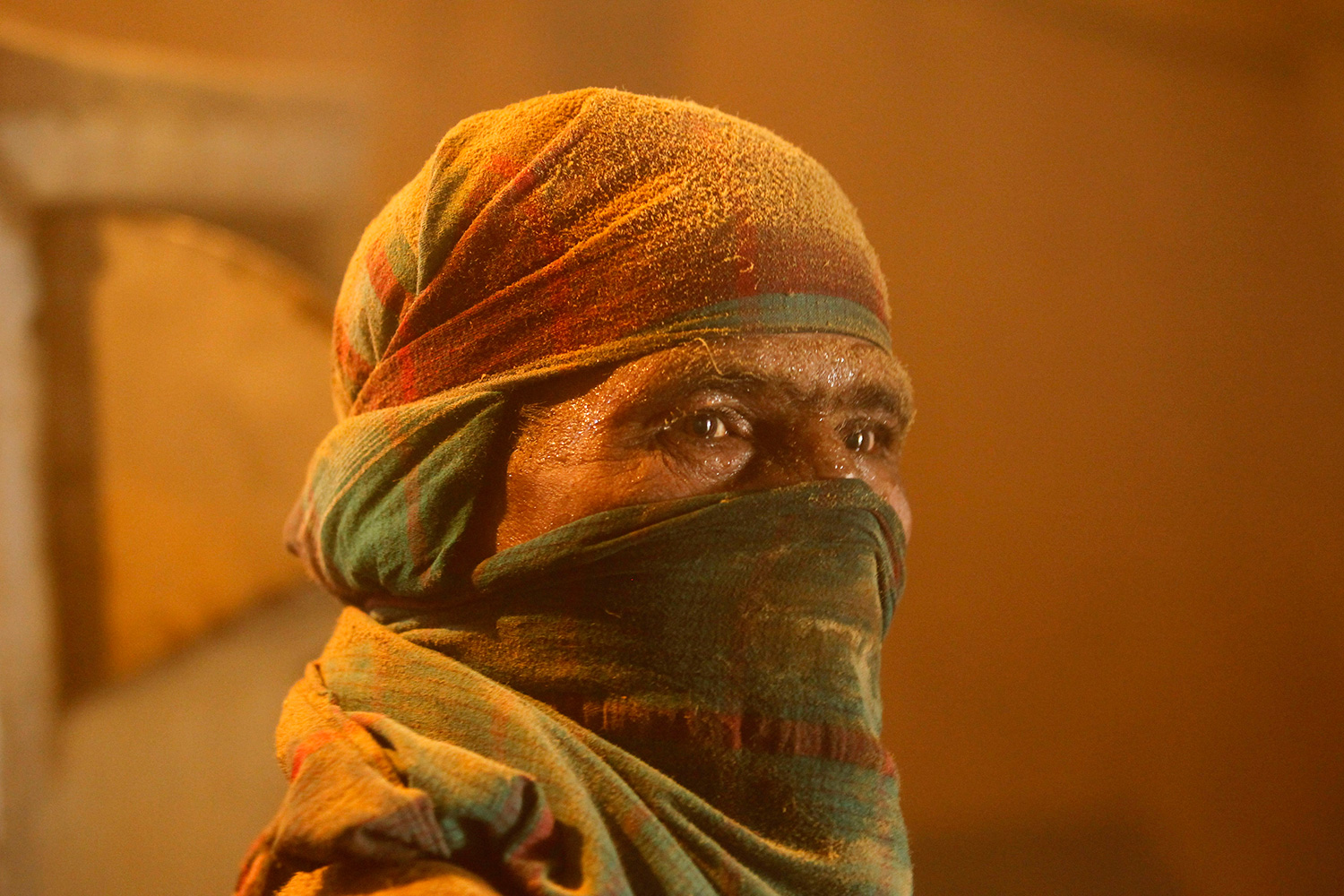 Picture shows the covered face of a woman in an orange glowing light.