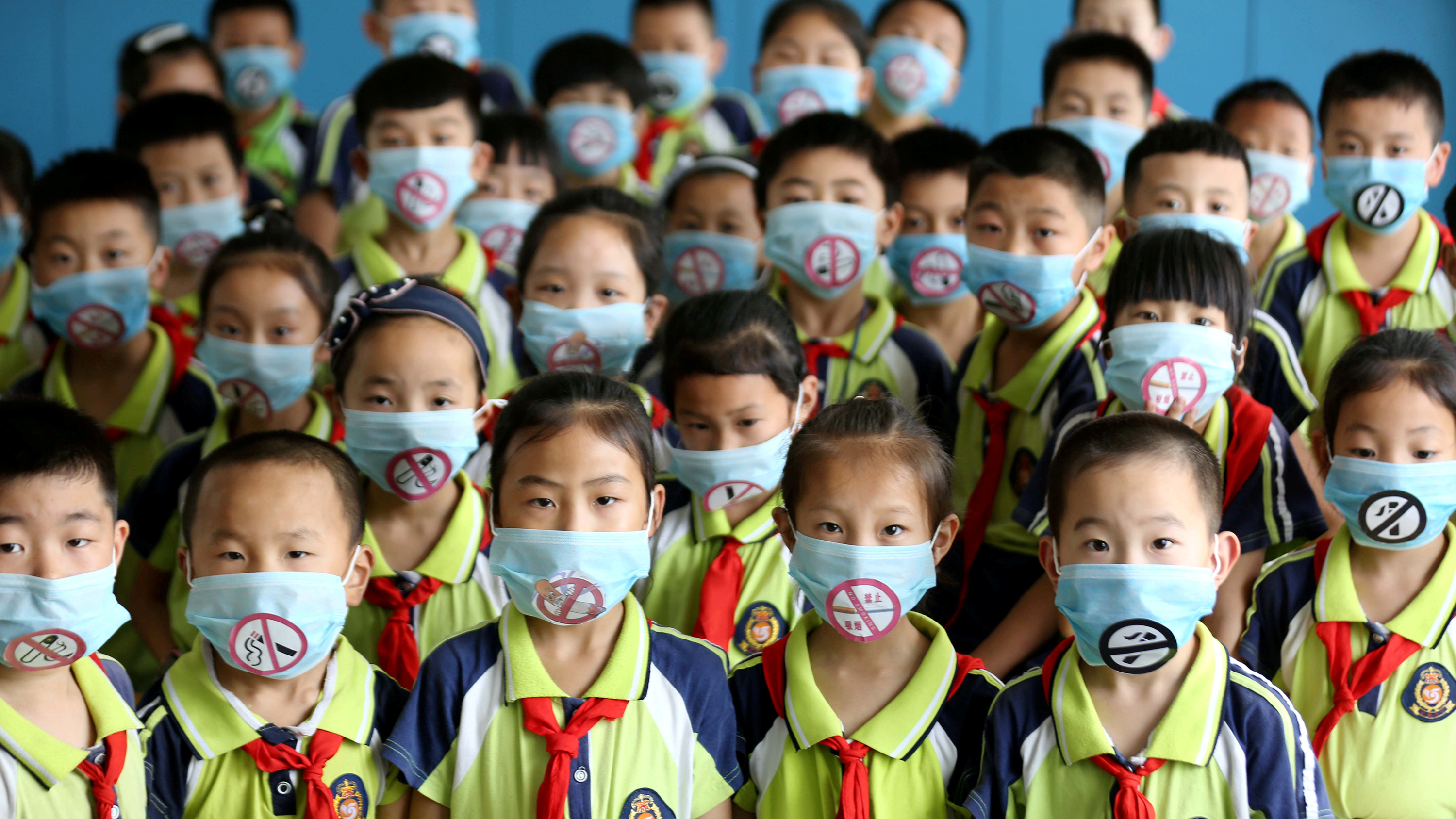 The photo shows a room full of children in school uniforms and no-smoking masks.