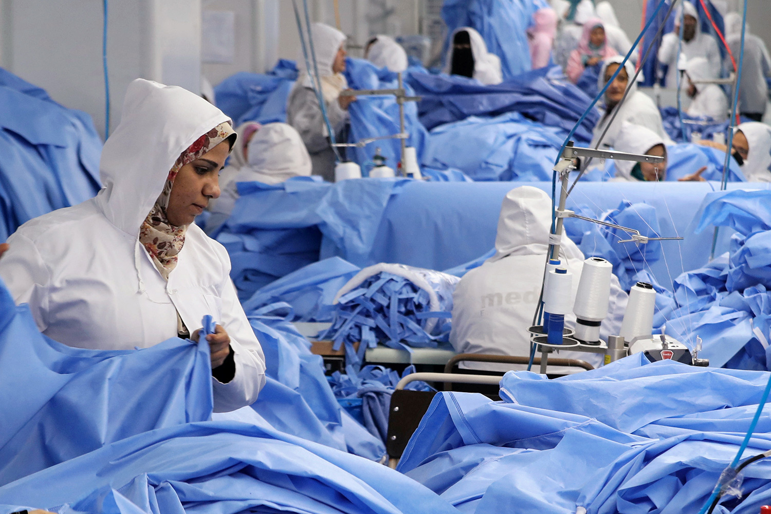 Picture shows blue—lots of blue. The workers are in white protective clothing in the factory assembly area, working among stacks of blue fabric.