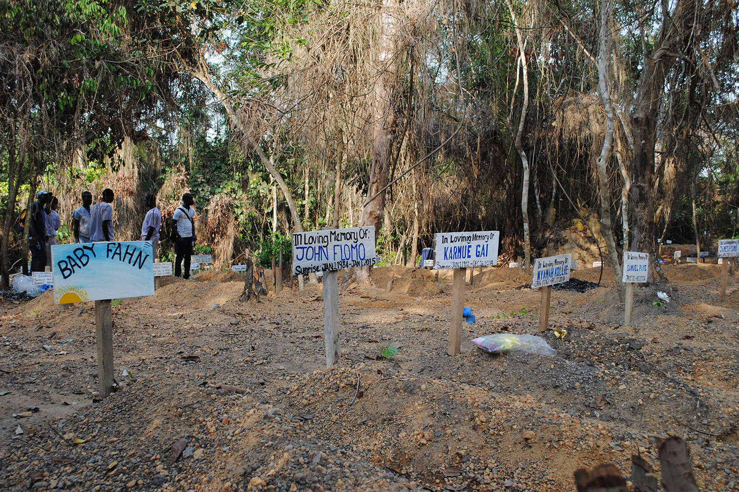 The graveyard has what appear to be freshly dug graves adorned with hand-painted wooden markers with names like "John Flomo" And "Baby Fahn."
