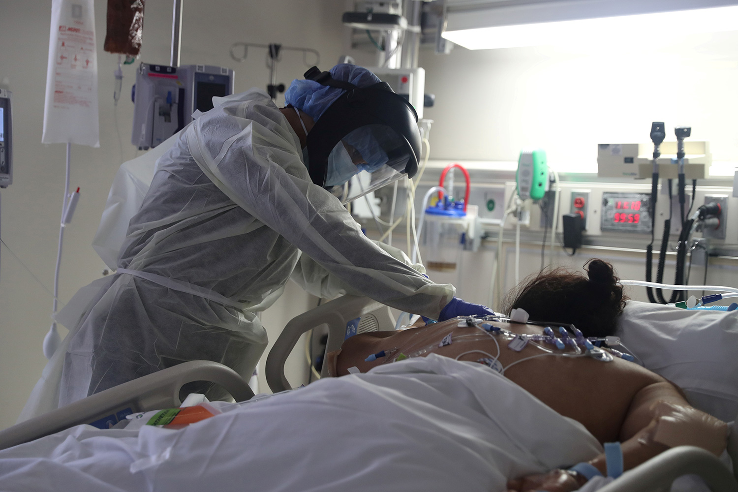 The photo shows a health care worker attending to a patient lying face down on the hospital bed.