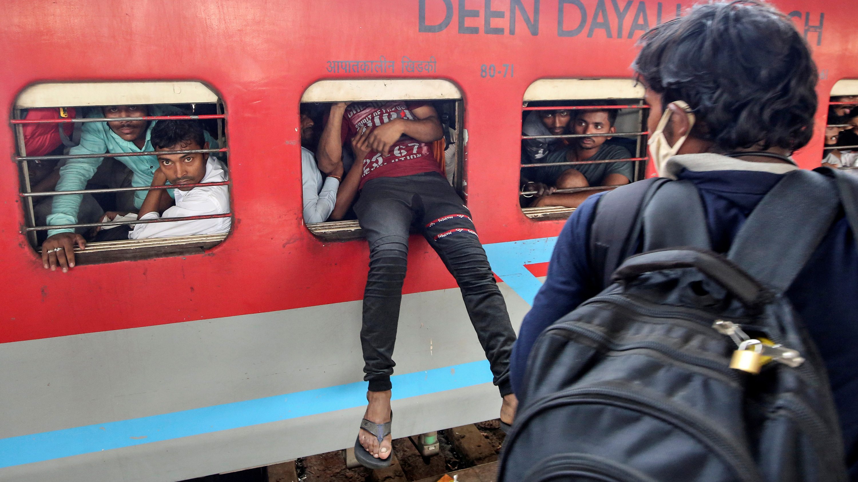 This is a striking photo of someone trying to scramble through the open window of a bright red passenger car on a train. Their legs from the waist down dangle precariously out the window.