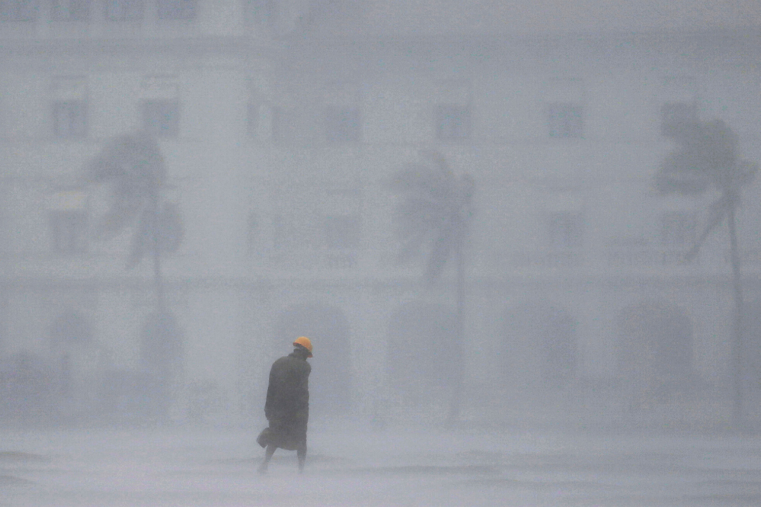 The picture shows a man from a distance walking down the street in a deluge of rainfall. It's raining so hard the man is barely visible in the camera.