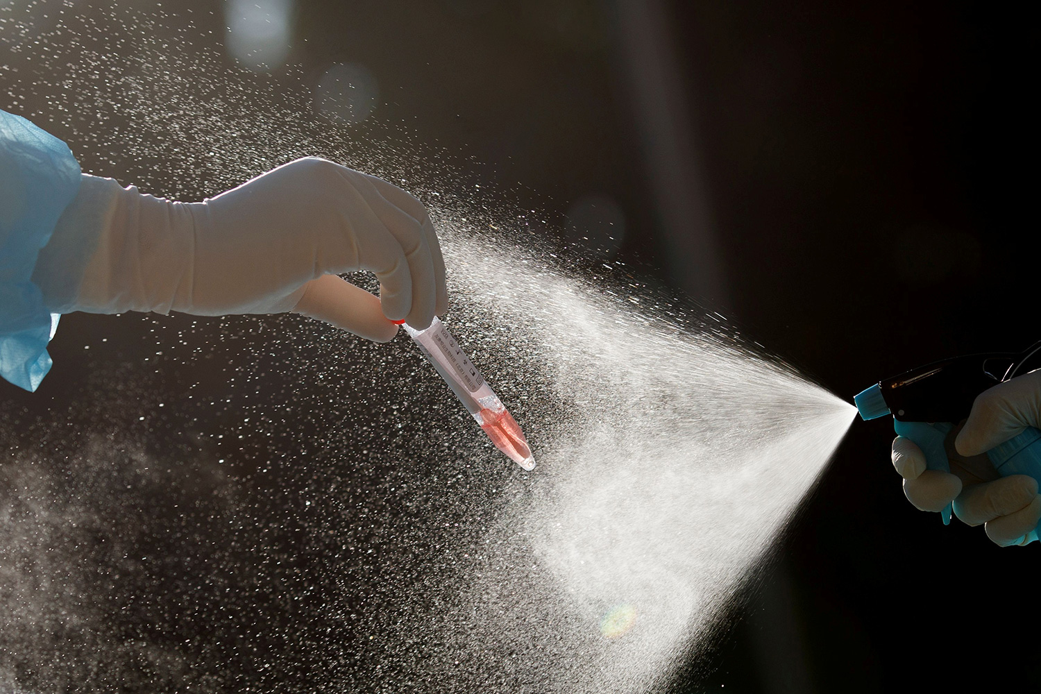 The photo shows one hand holding a small vial with a fluid that appears to be blood while another hand sprays a mist over the whole thing.