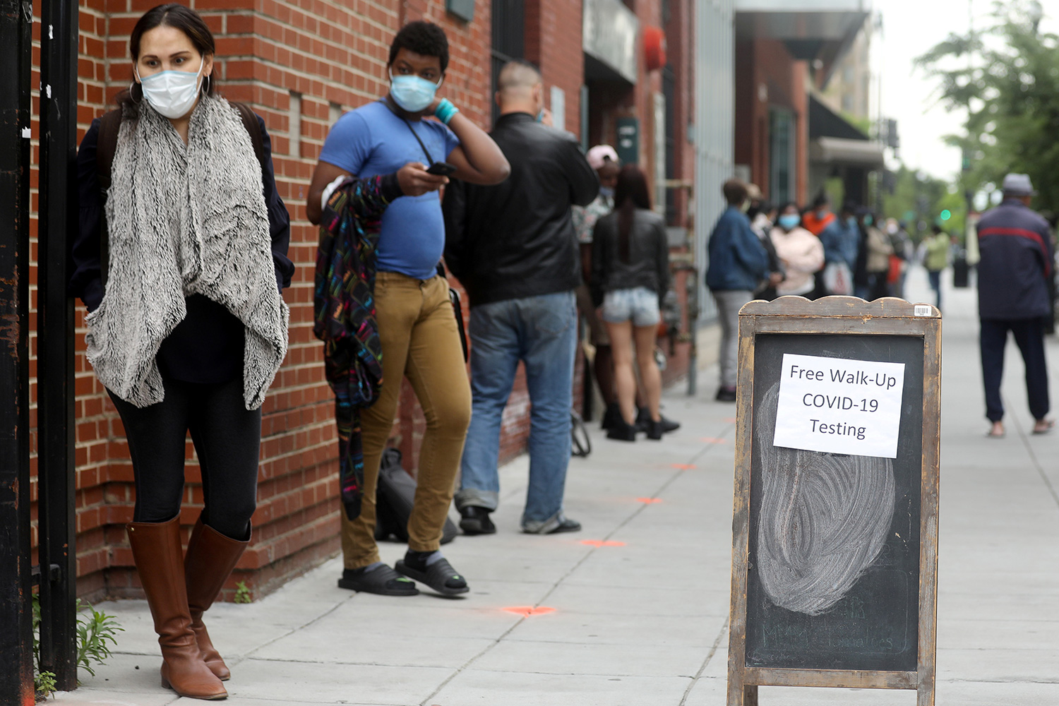 The photo shows a long line of people waiting. The woman in the very front is staring off into space in apparent disbelief.