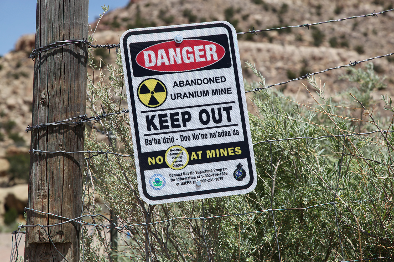 Picture shows a sign on a fence in a remote-looking desert area warning people to "KEEP OUT" because of the dangers.