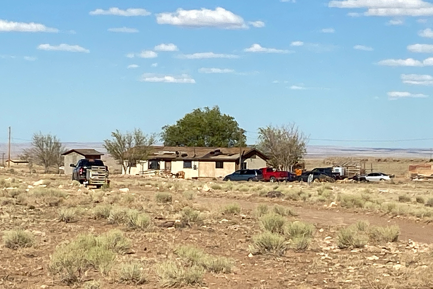 Picture shows a rural home on a beautiful spring day from a distance. Several cars and trucks can be seen outside.