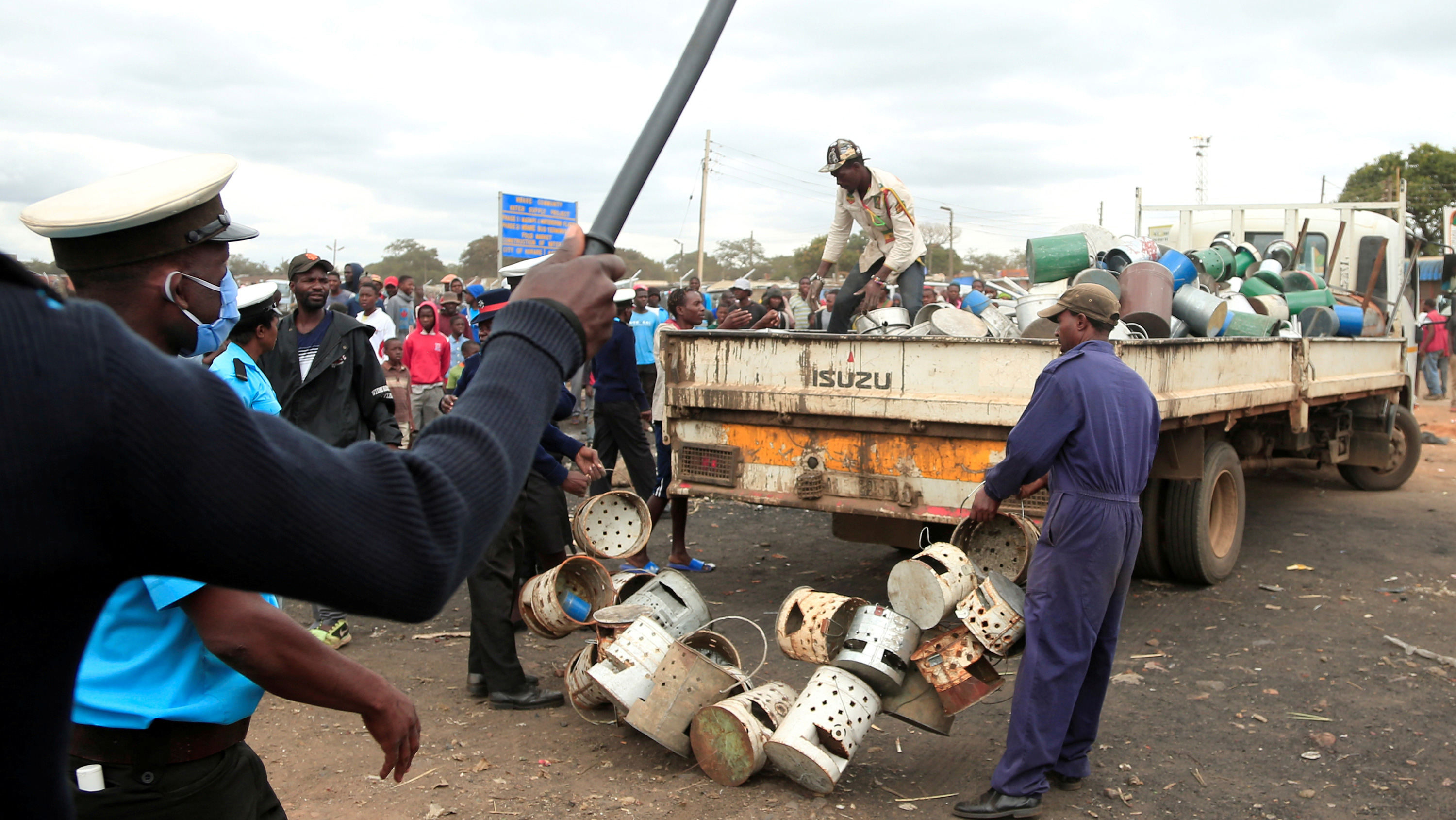 The photo shows a chaotic scene with a police officer waving a baton and people dragging crates and barrels onto a truck.