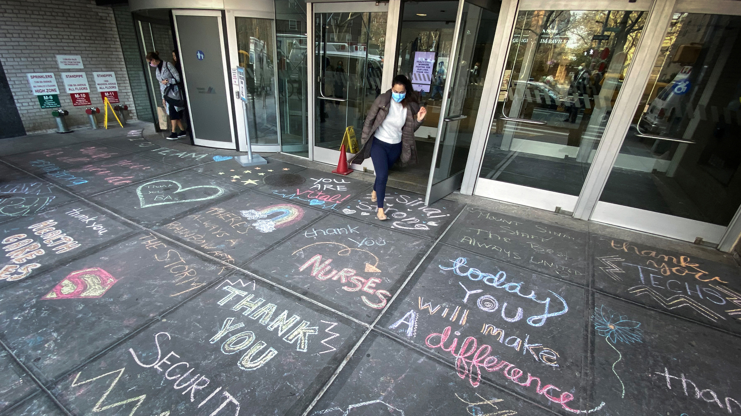 The photo shows an entrance to the hospital with a large number of colorful messages of thanks written in chalk on the sidewalk outside.
