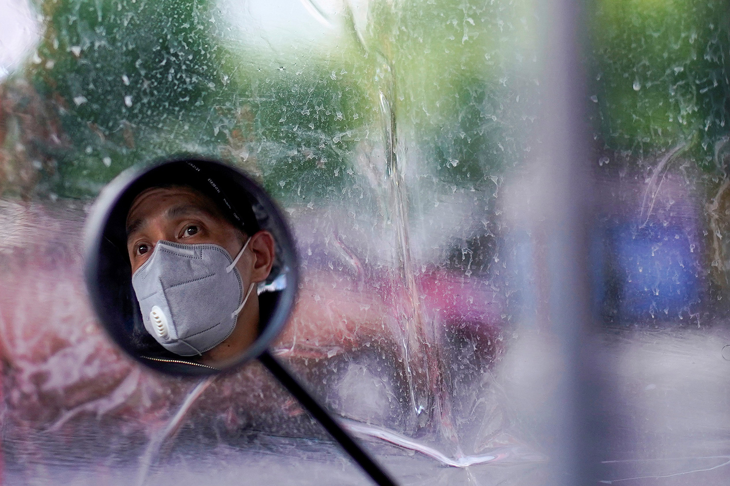 This is a striking photo showing a blurred out background against which stands a single, small round rear view mirror and the man's face wearing a mask within.