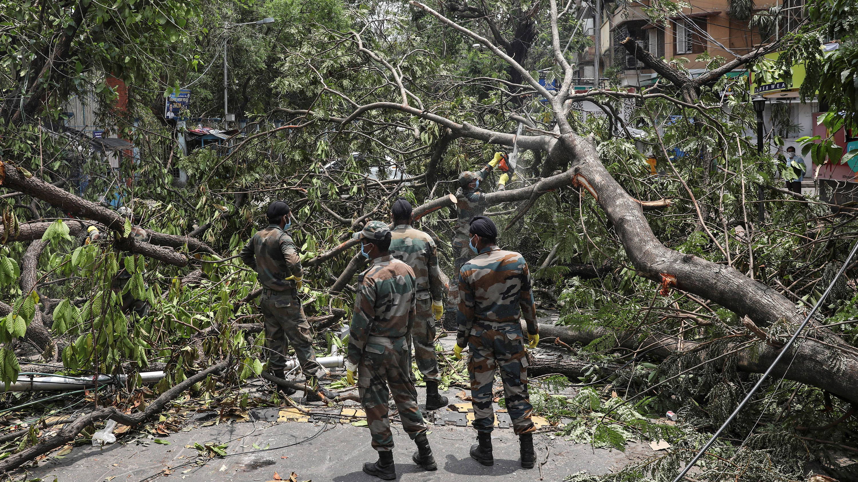 The photo shows several soldiers standing amid fallen trees and other storm-related destruction.
