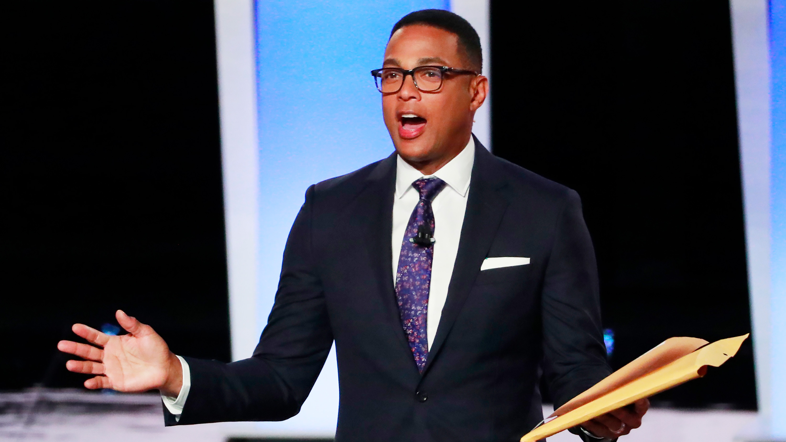 The photo shows the journalist in a smart suit speaking and gesturing with his hands.