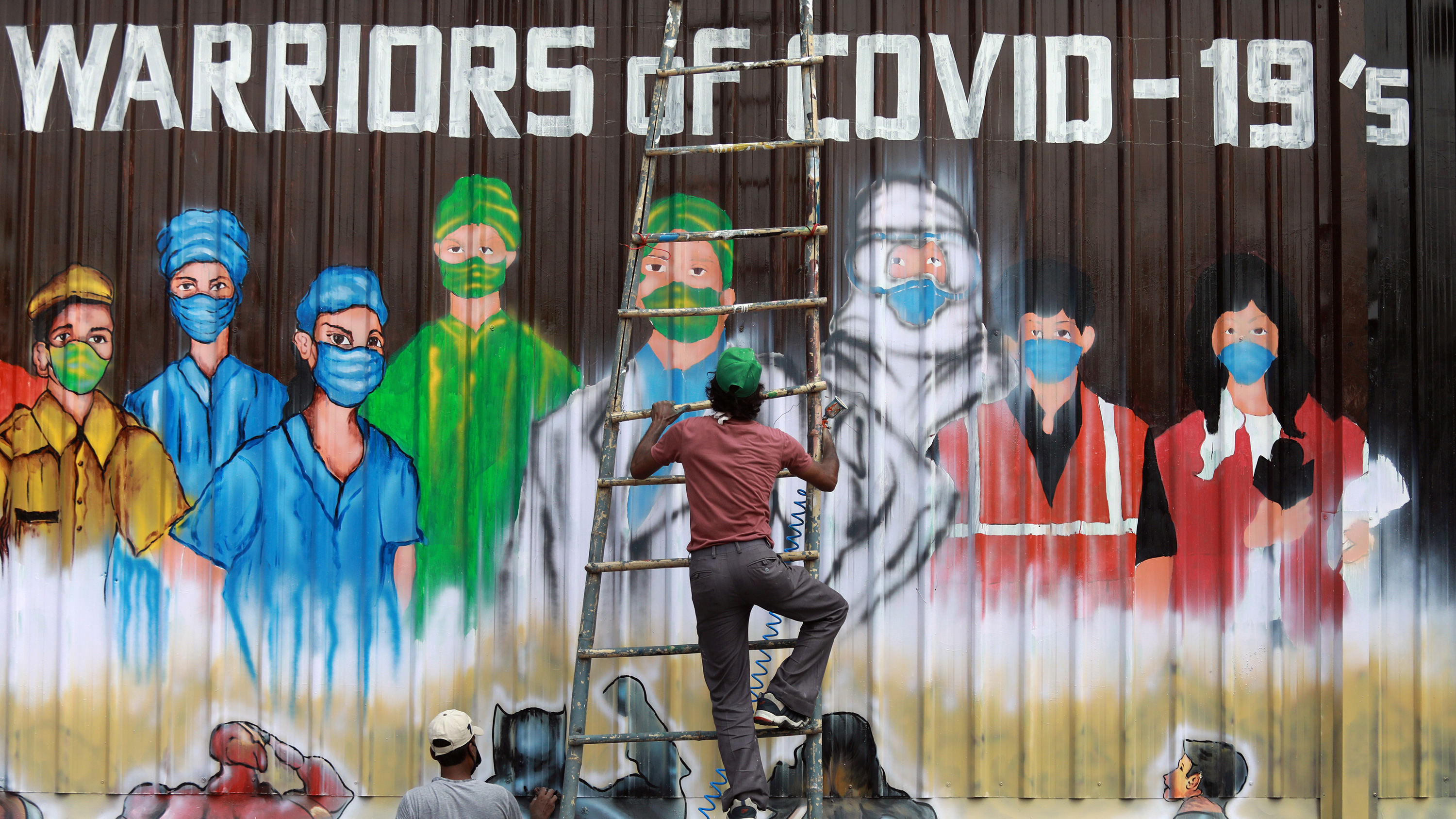 Image shows the artist coming down off the ladder in front of his mural to doctors, nurses, and other health workers.