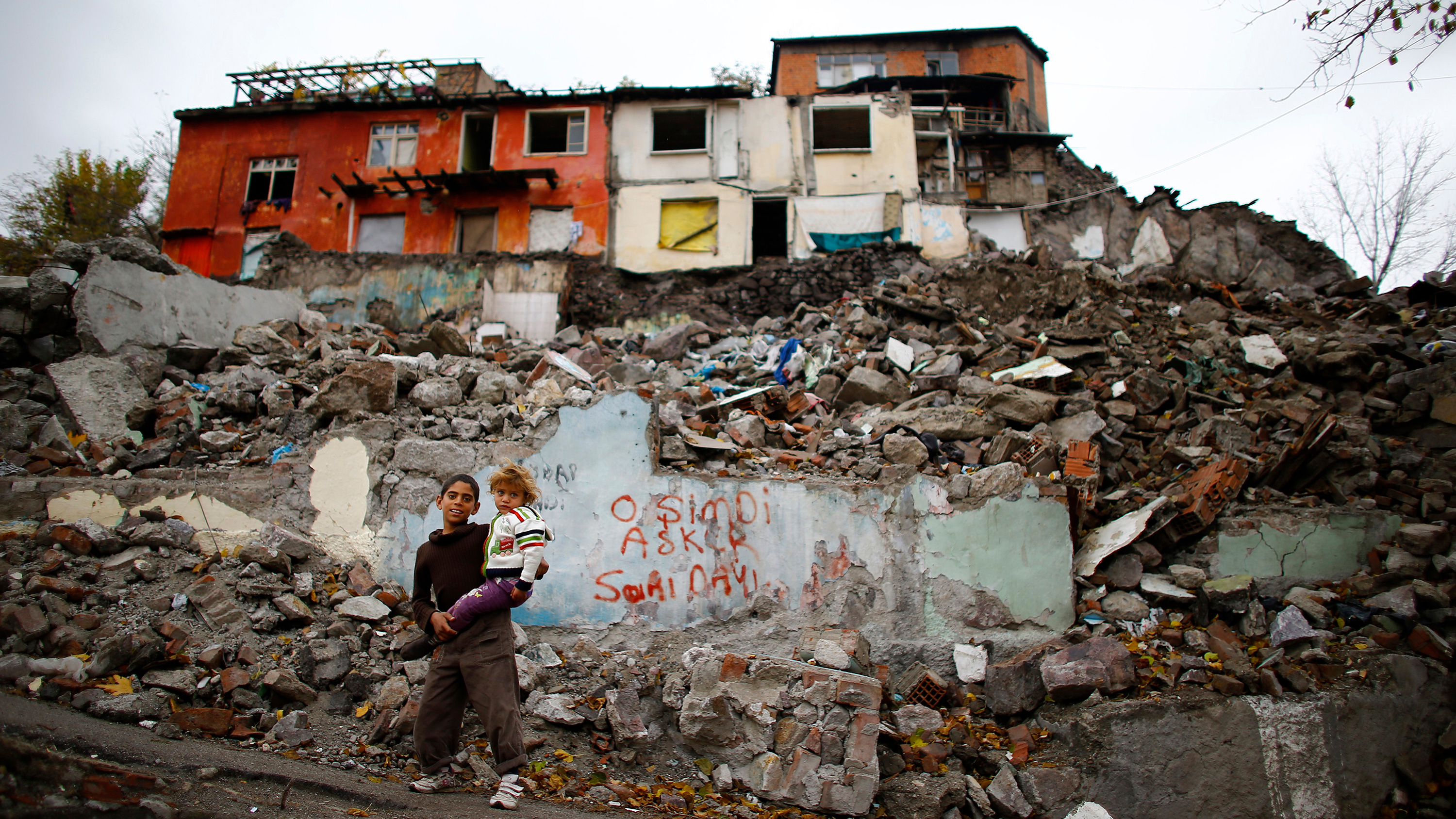The graffiti reads, "He is now a soldier." Picture shows a boy holding his sister amid a crumbling, poor housing area.
