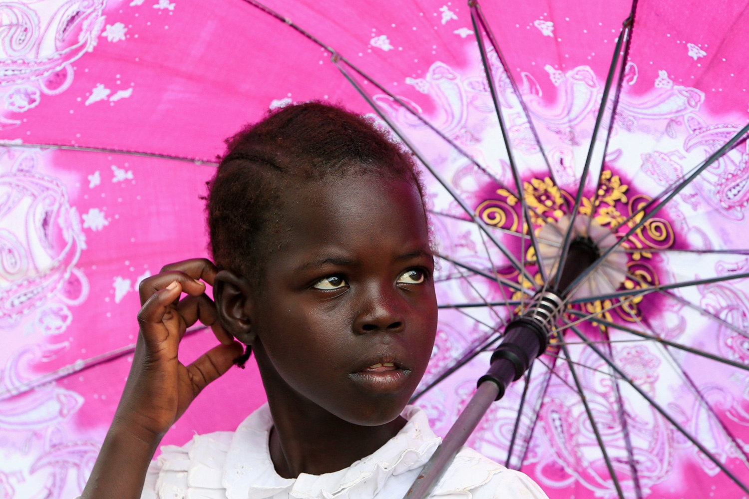 Picture shows a girl looking to her left standing under a pink umbrella.