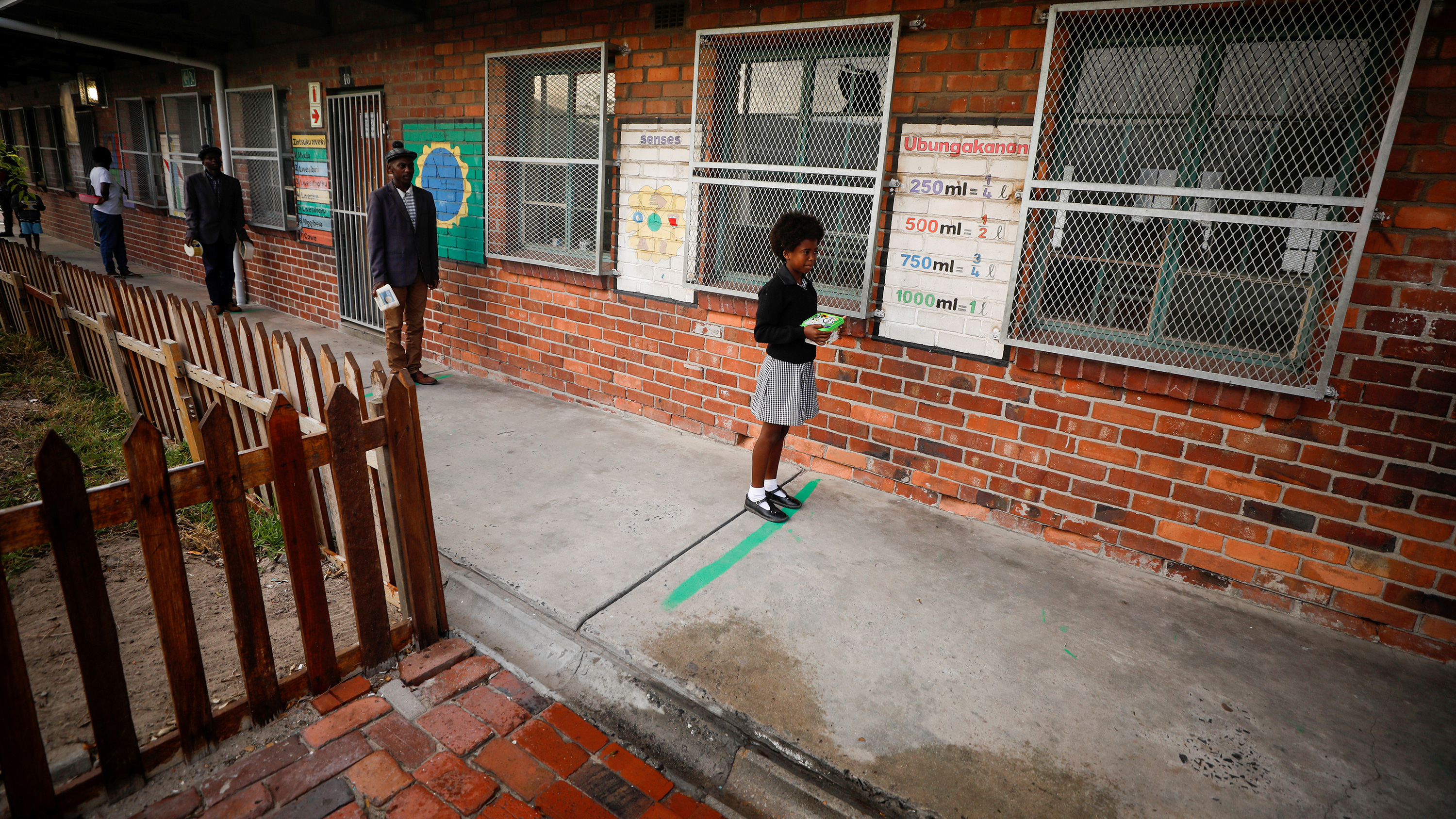 Picture shows several children lined up along the side of a low-rise building. 