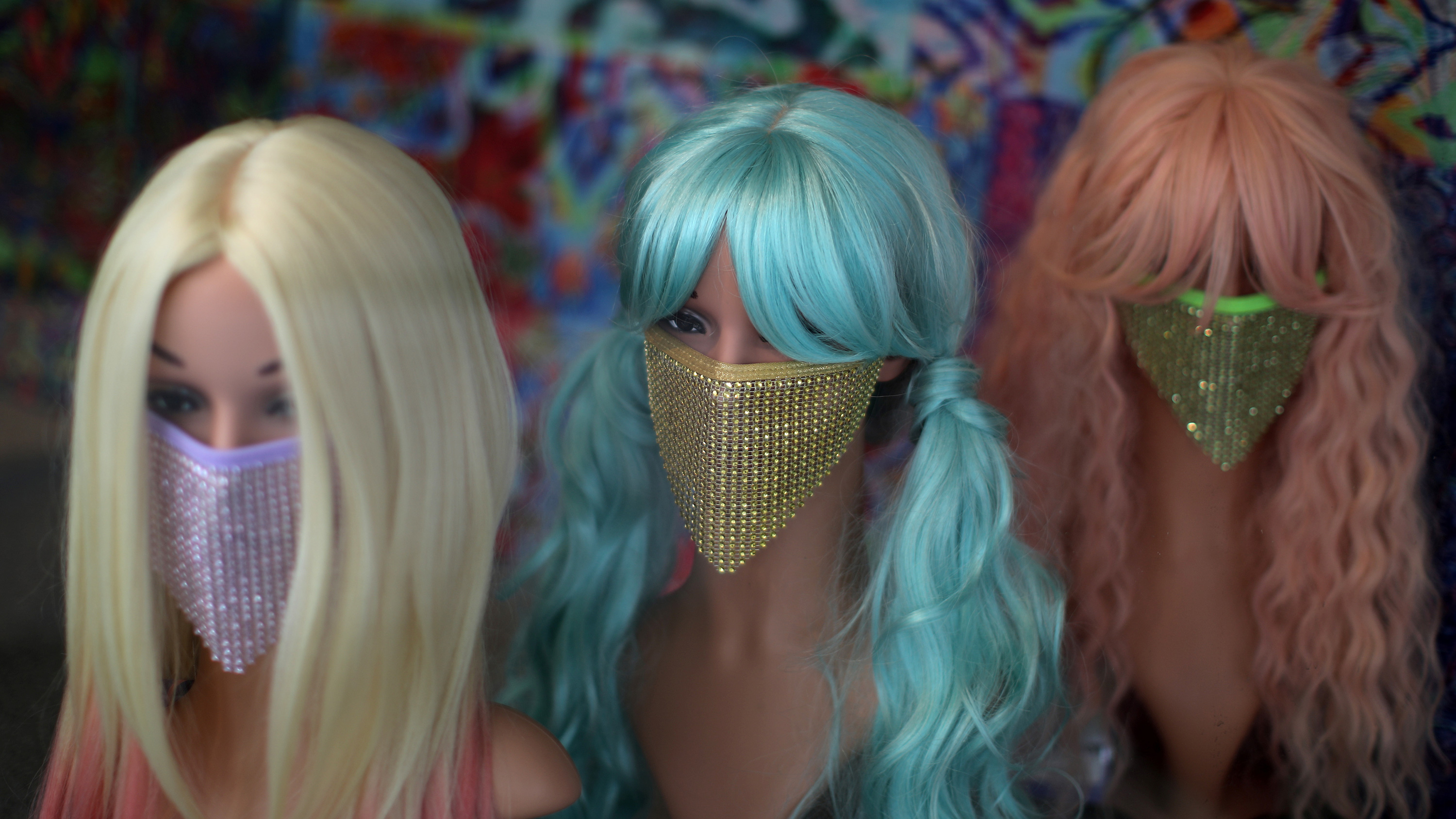 The photo shows three mannequin heads, each with a colorful wig as well as a colorful, sequined mask.