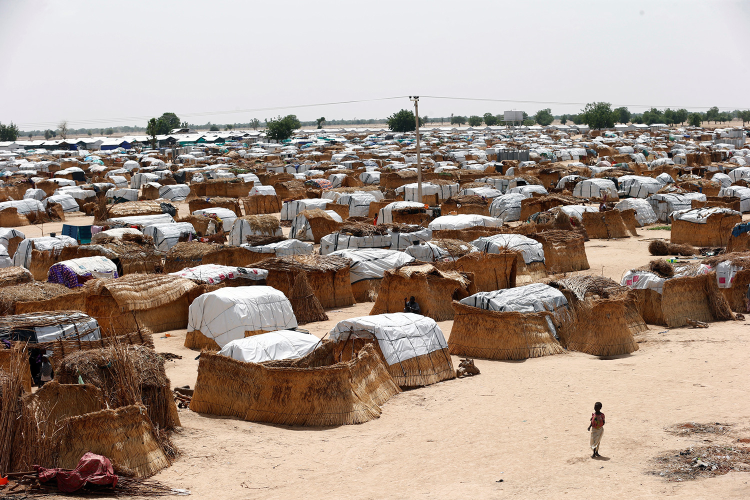 The photo shows a small girl in the foreground against the backdrop of a massive camp.