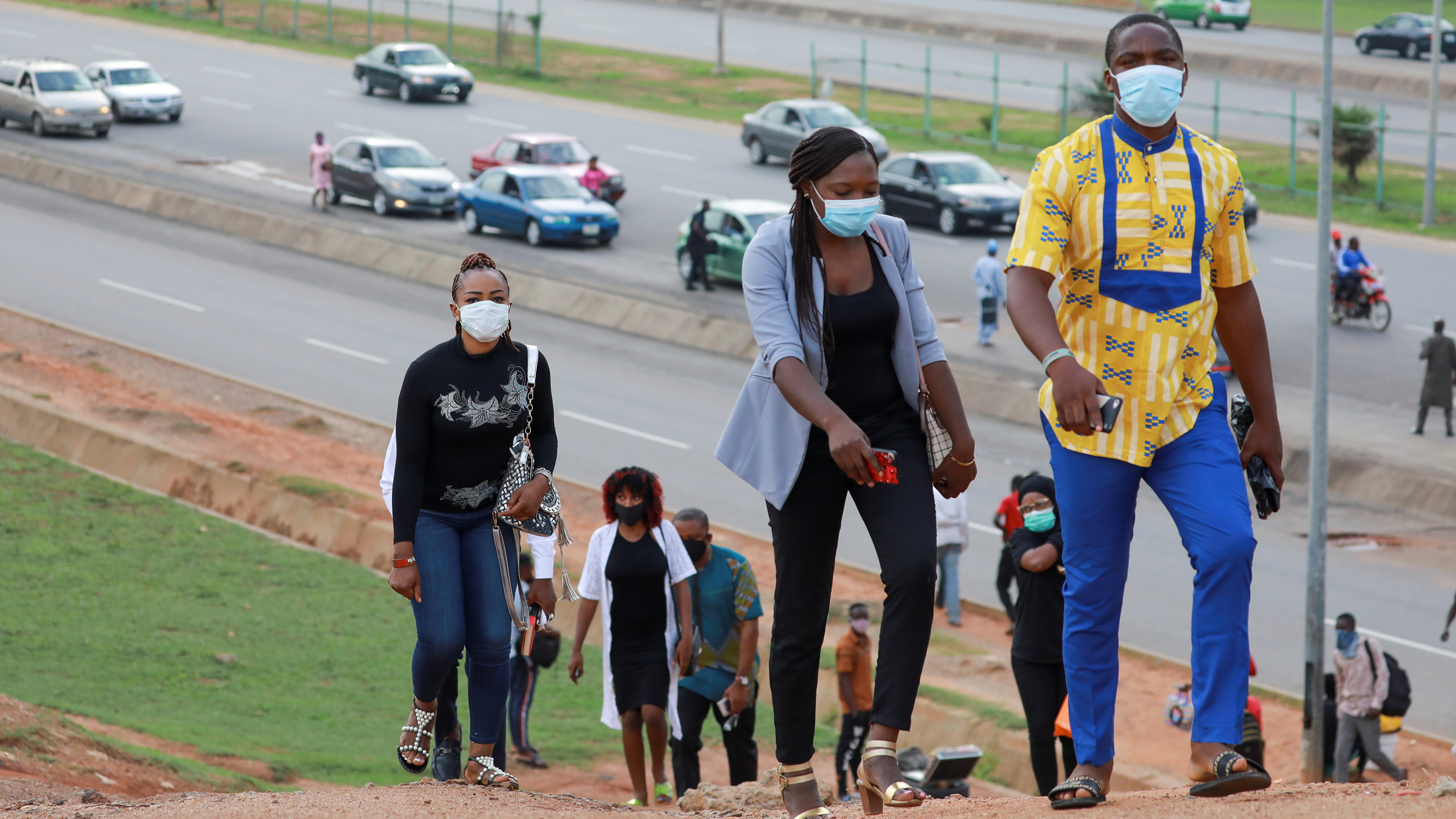 The photo shows a number of people walking up a steep slope of a hill overlooking a busy street.