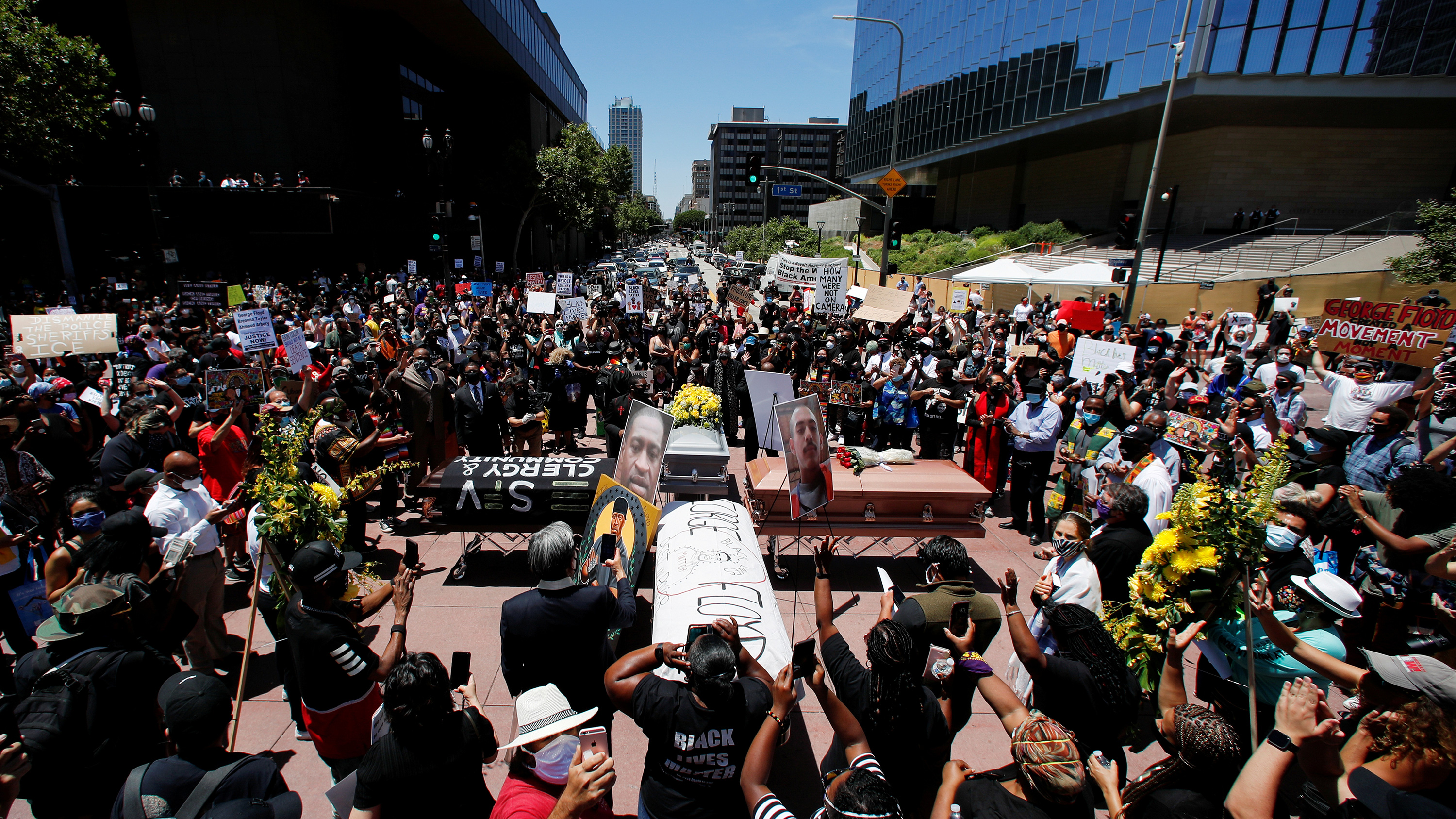 The photo shows a large crowd gathered around some coffins arranged in a cross-like formation.