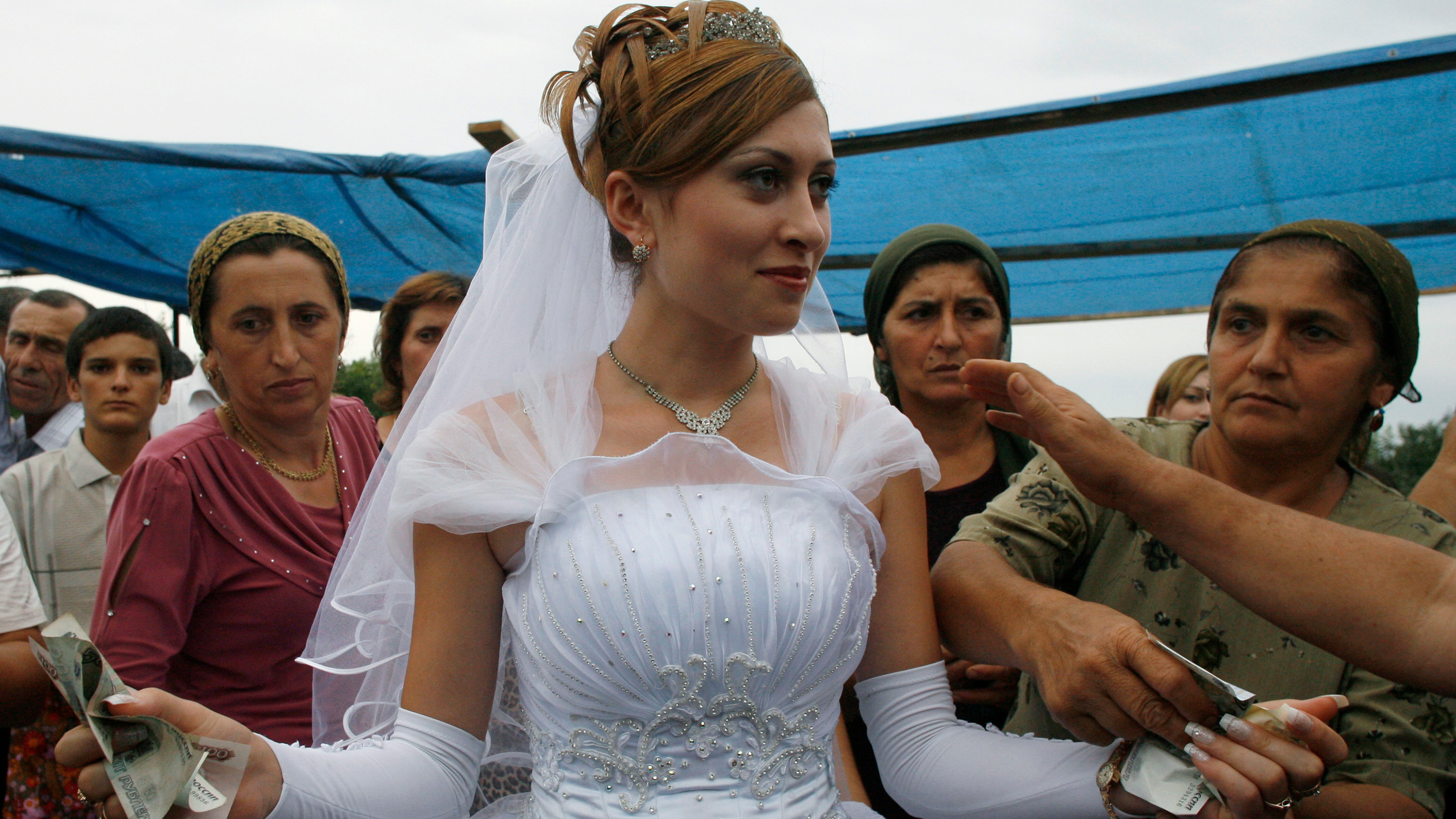 The photo shows a bride at the center of the frame surrounded by older women.